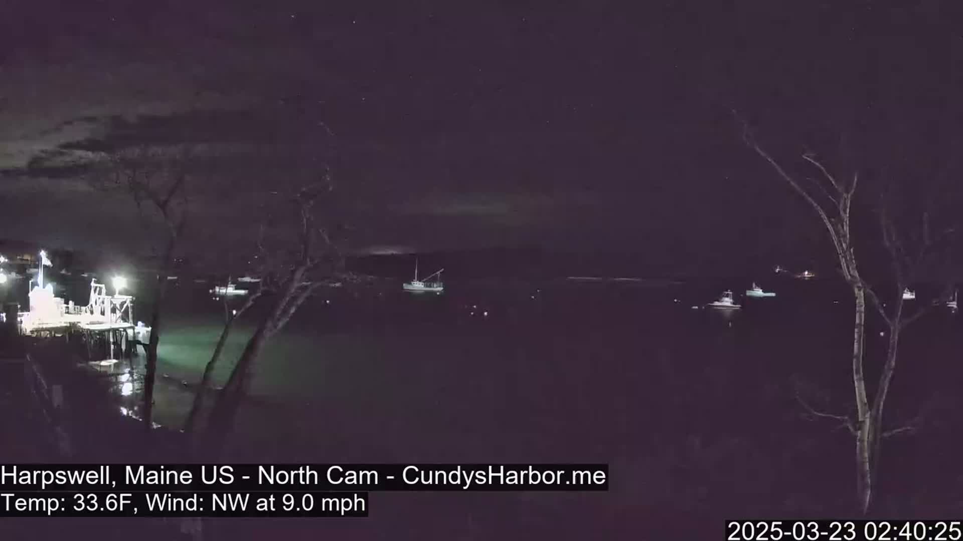 A nighttime view of a harbor with several boats moored, under a clear, starry sky and a northwest wind.
