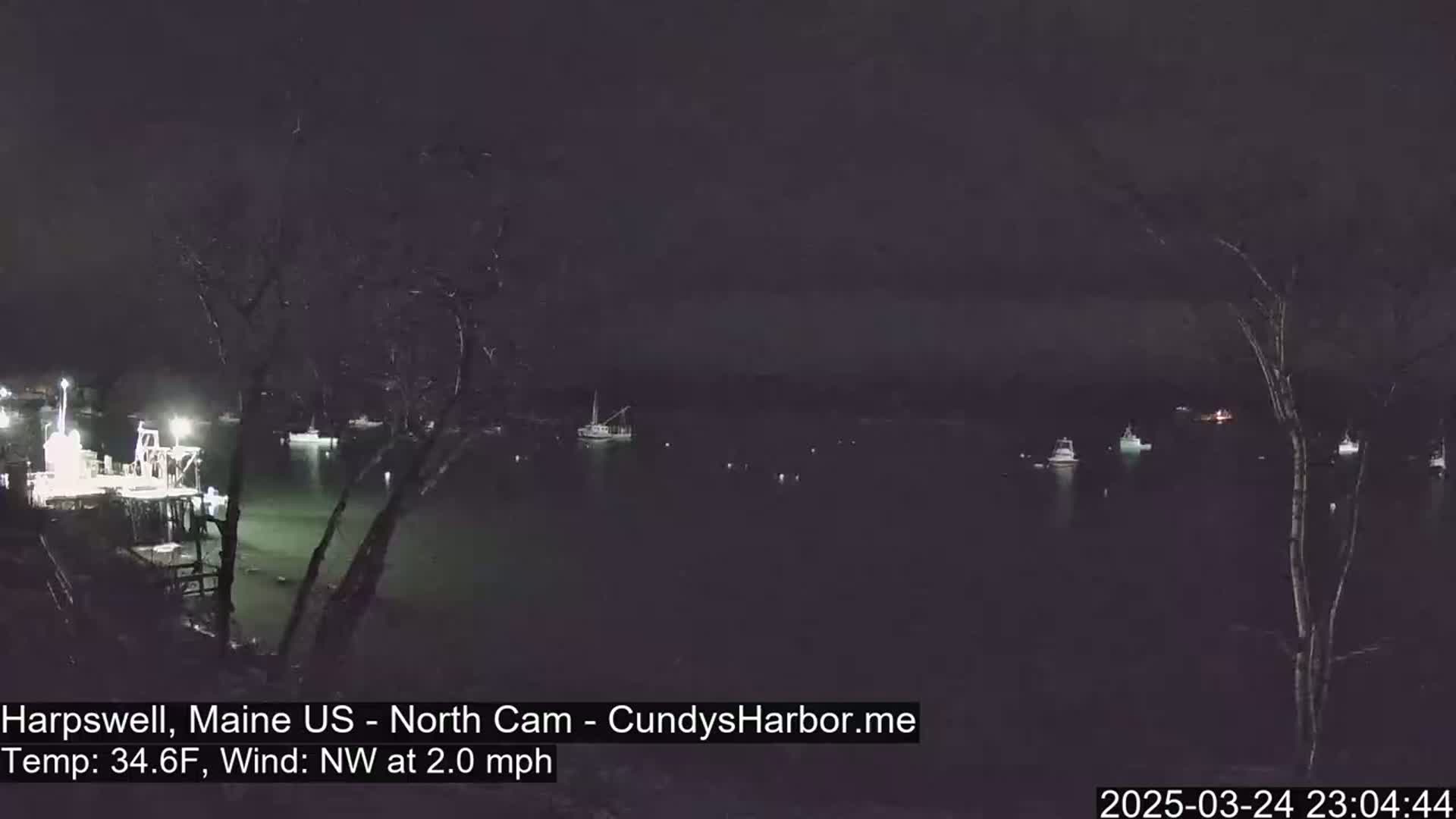 A nighttime view of a harbor with several boats moored, under a dark sky with a northwest wind blowing at 2.0 mph.