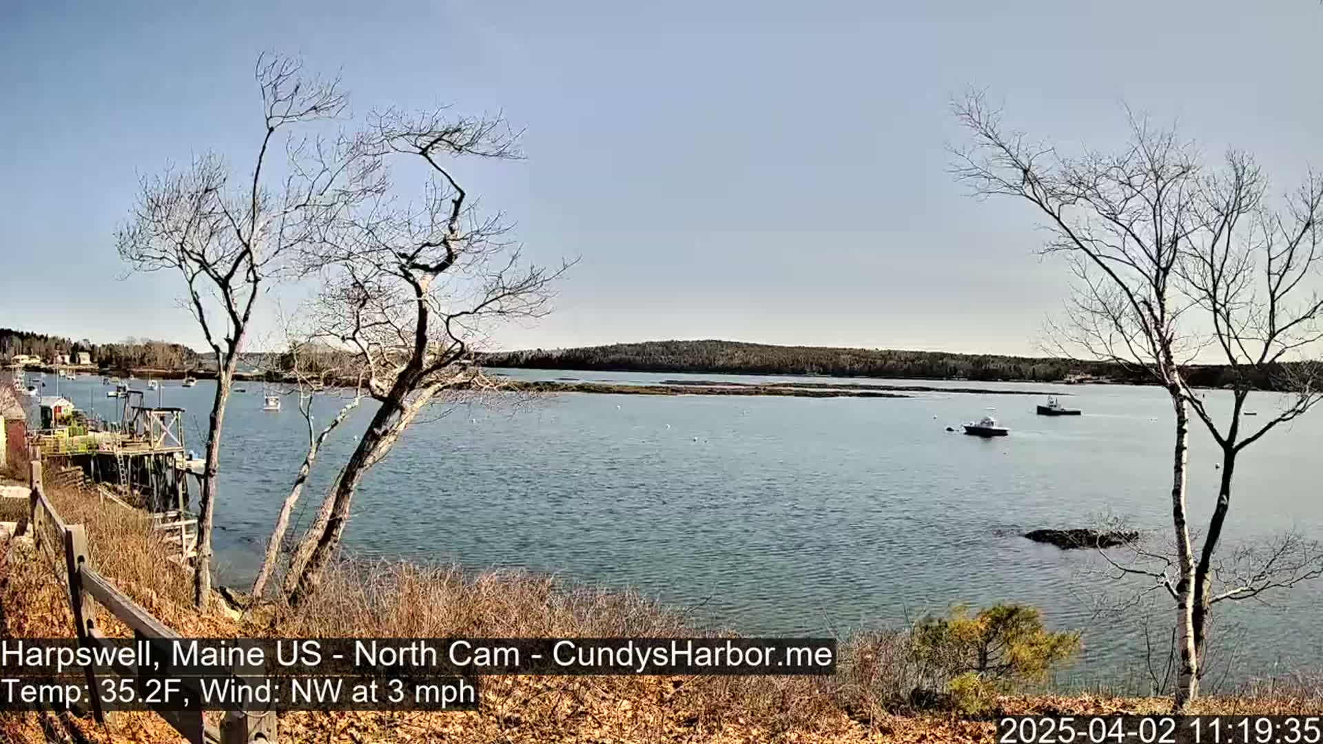A calm body of water with several boats, viewed from a slightly elevated vantage point on a clear, sunny day with a light northwest wind.