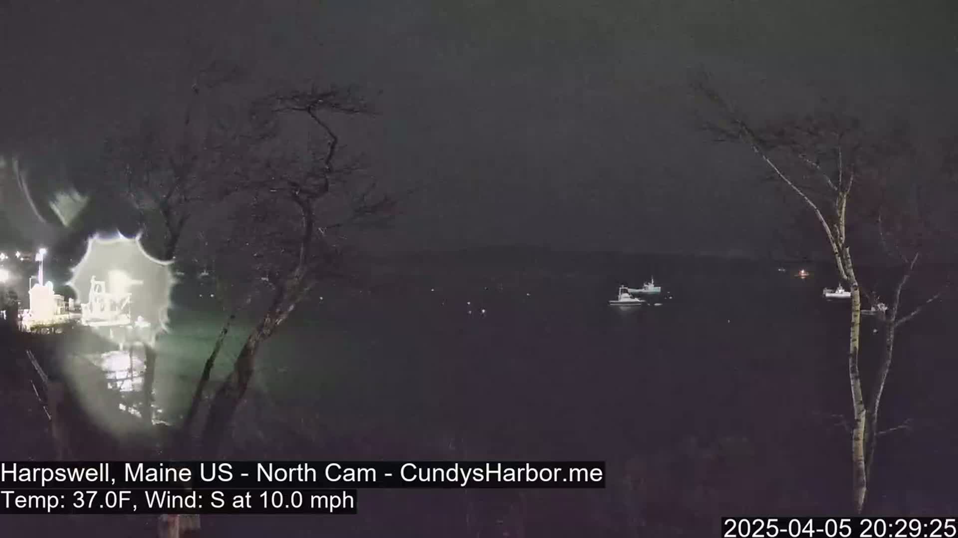 A nighttime view of a dark body of water with a few boats, silhouetted against a dark sky, under a 37°F temperature with a 10 mph south wind.