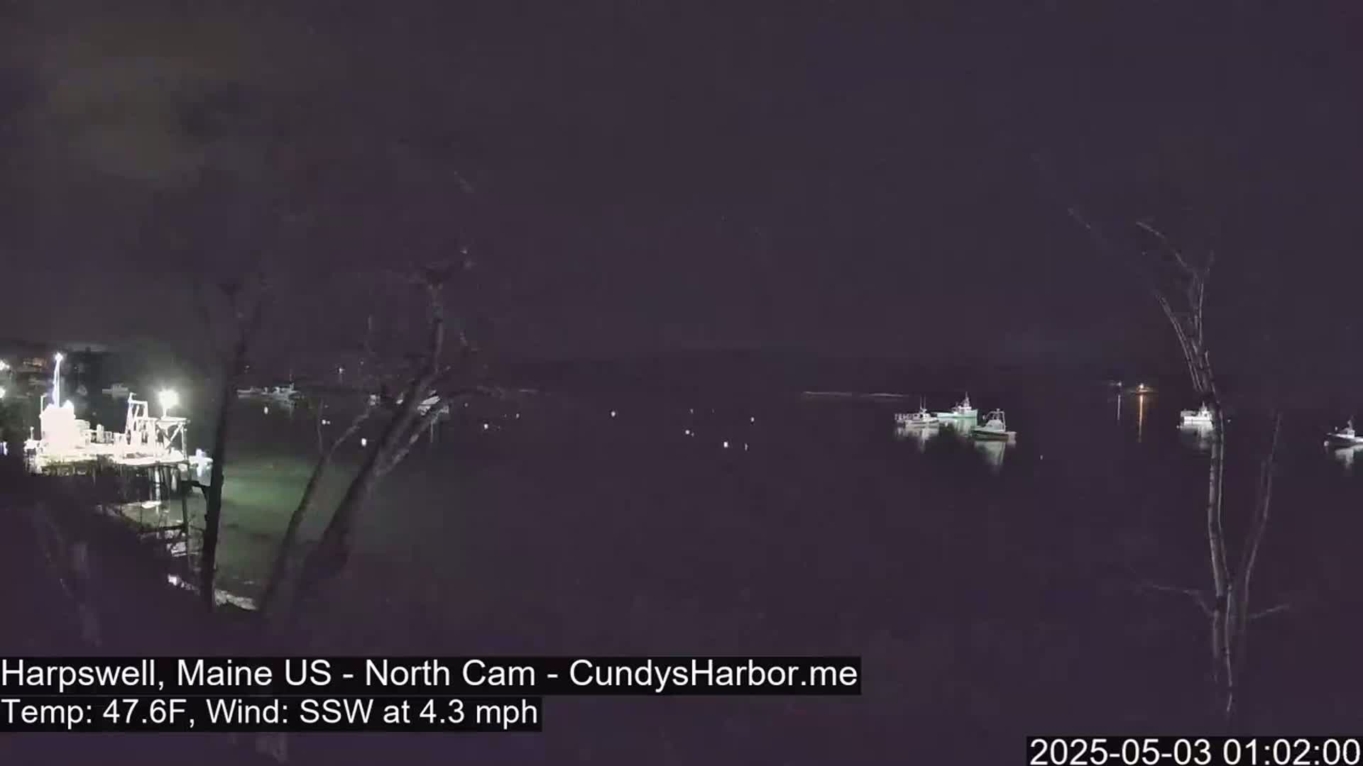 At night, several boats are moored in a dark harbor under a clear, dark sky with a slight south-southwesterly wind.