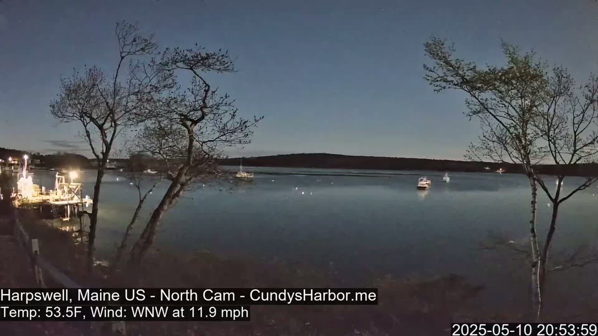 A moonlit harbor scene at night shows several boats on calm water, under a dark blue sky with a WNW wind at 11.9 mph and a temperature of 53.5°F.