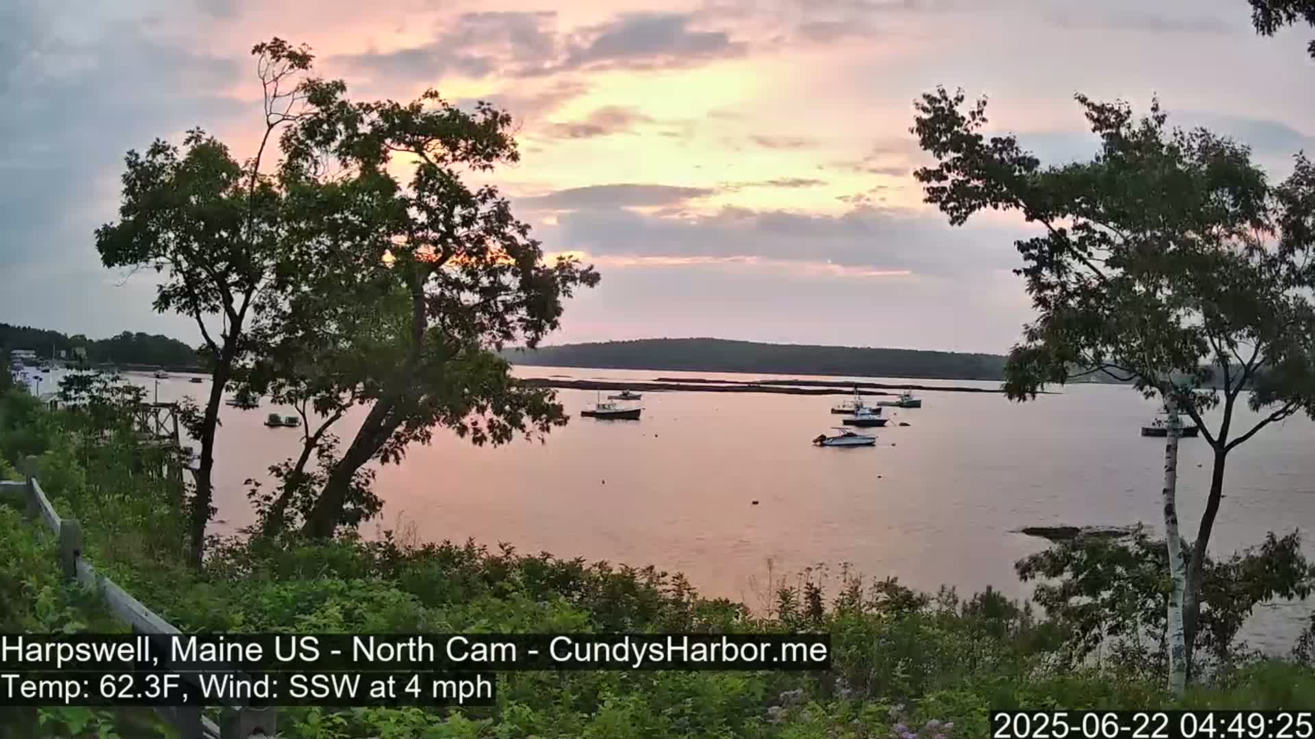 Several boats are moored in a calm bay at sunset under a partly cloudy sky.