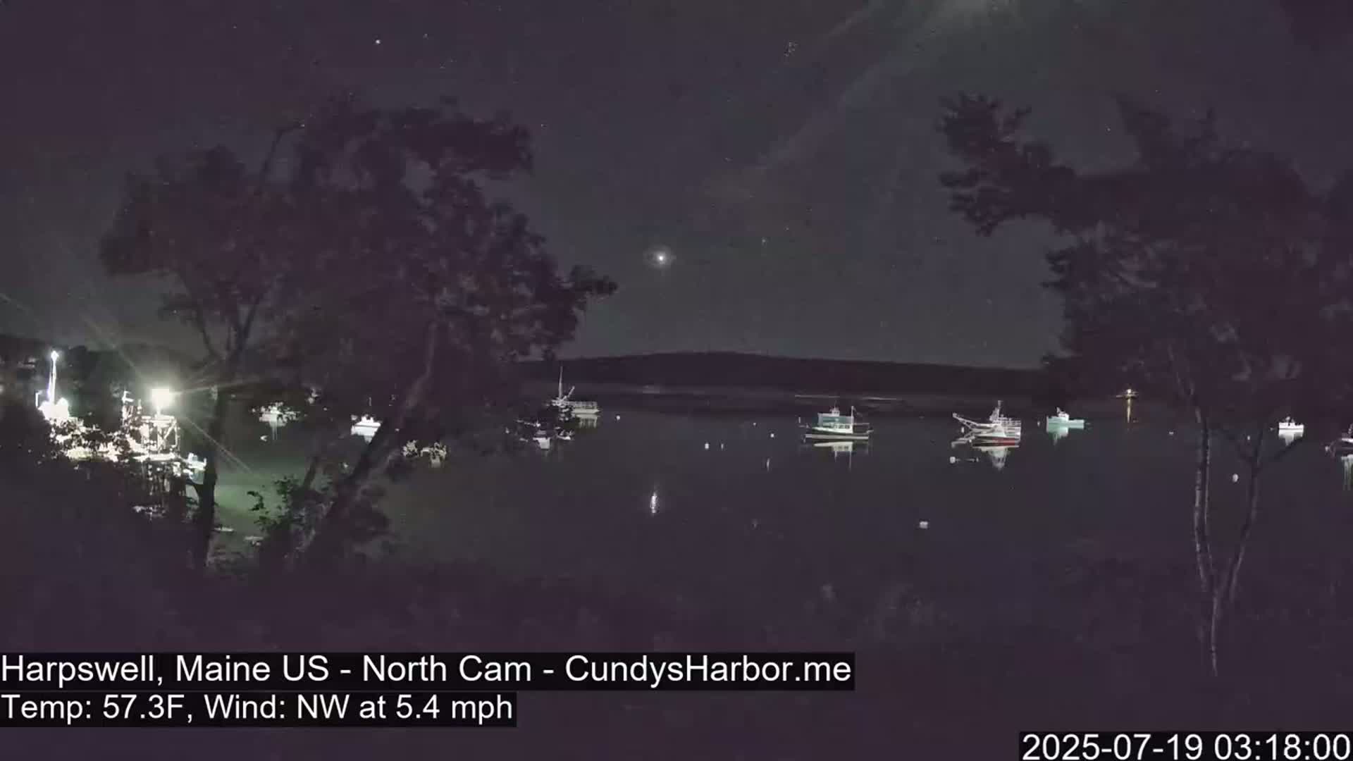 Several boats are moored in a calm, dark harbor under a clear, starry night sky.