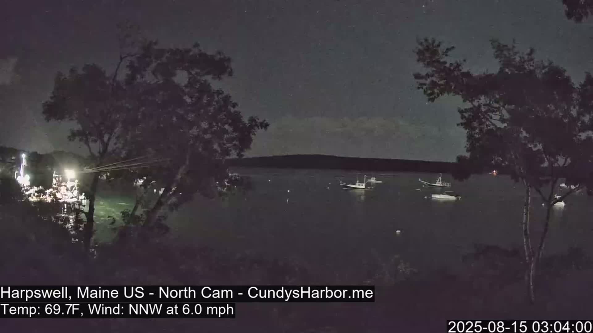 Several boats are moored in a dark body of water at night under a mostly clear sky, with a gentle northwest wind.
