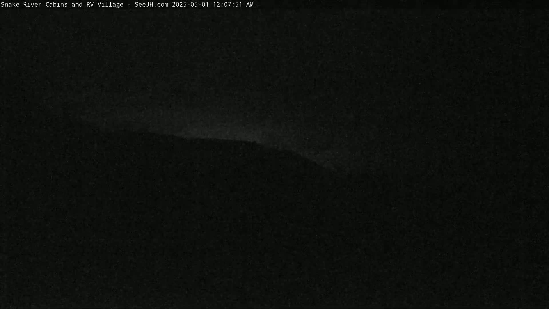 A dark, nighttime image shows a faintly illuminated hill or mountain range under a mostly clear sky.