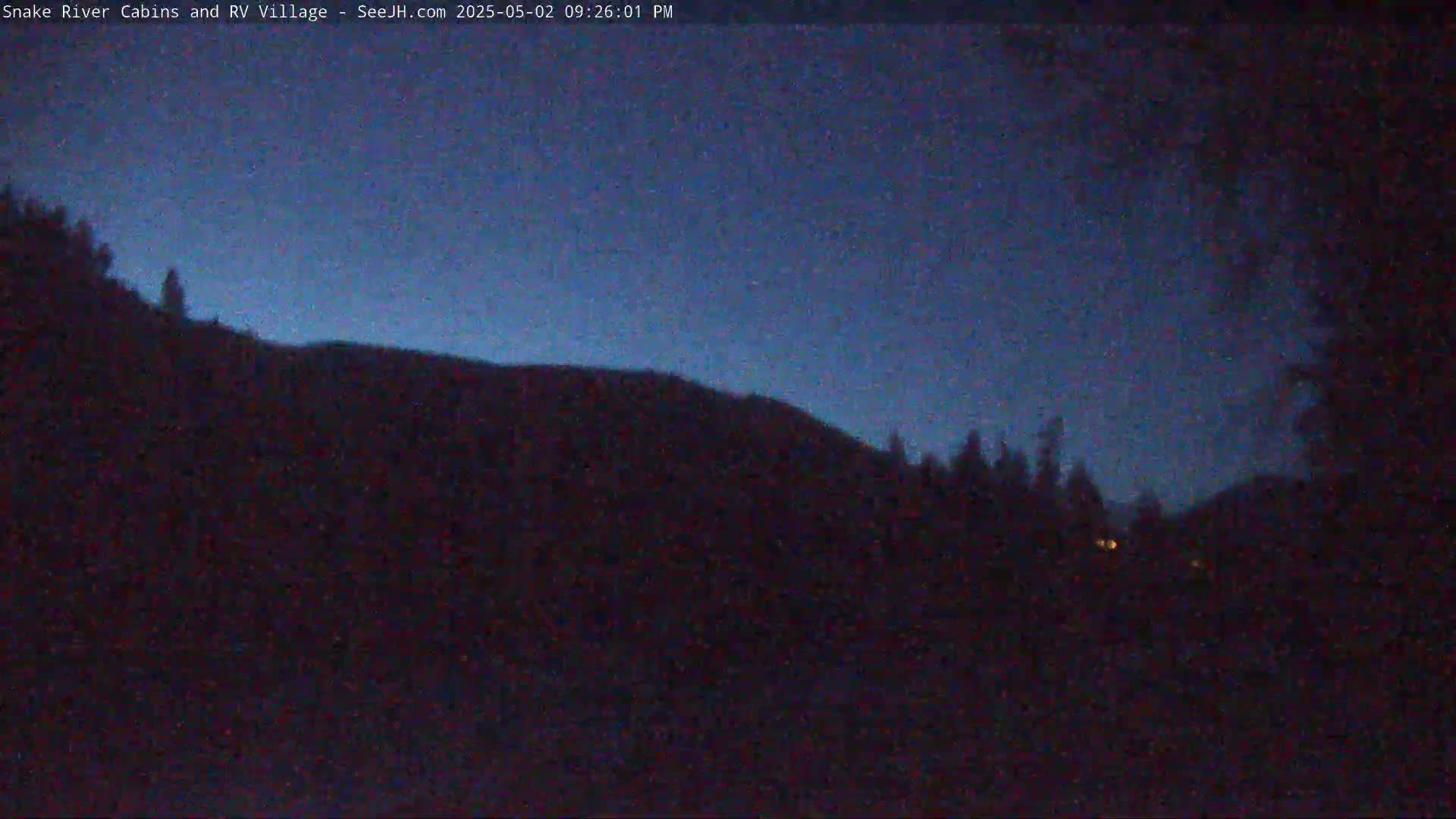 A dark, silhouetted hill and trees are visible under a twilight blue sky.
