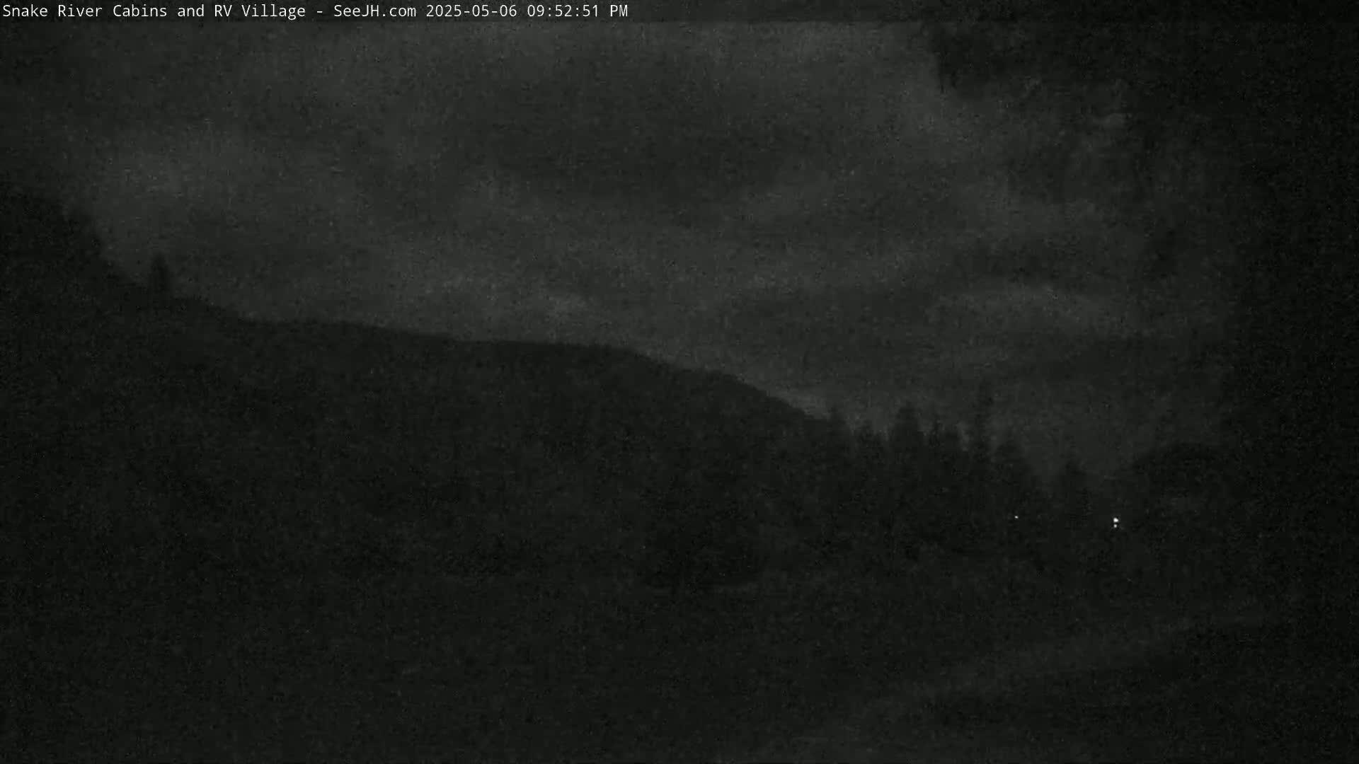 A dark, nighttime scene shows a hill covered in trees under a cloudy sky.