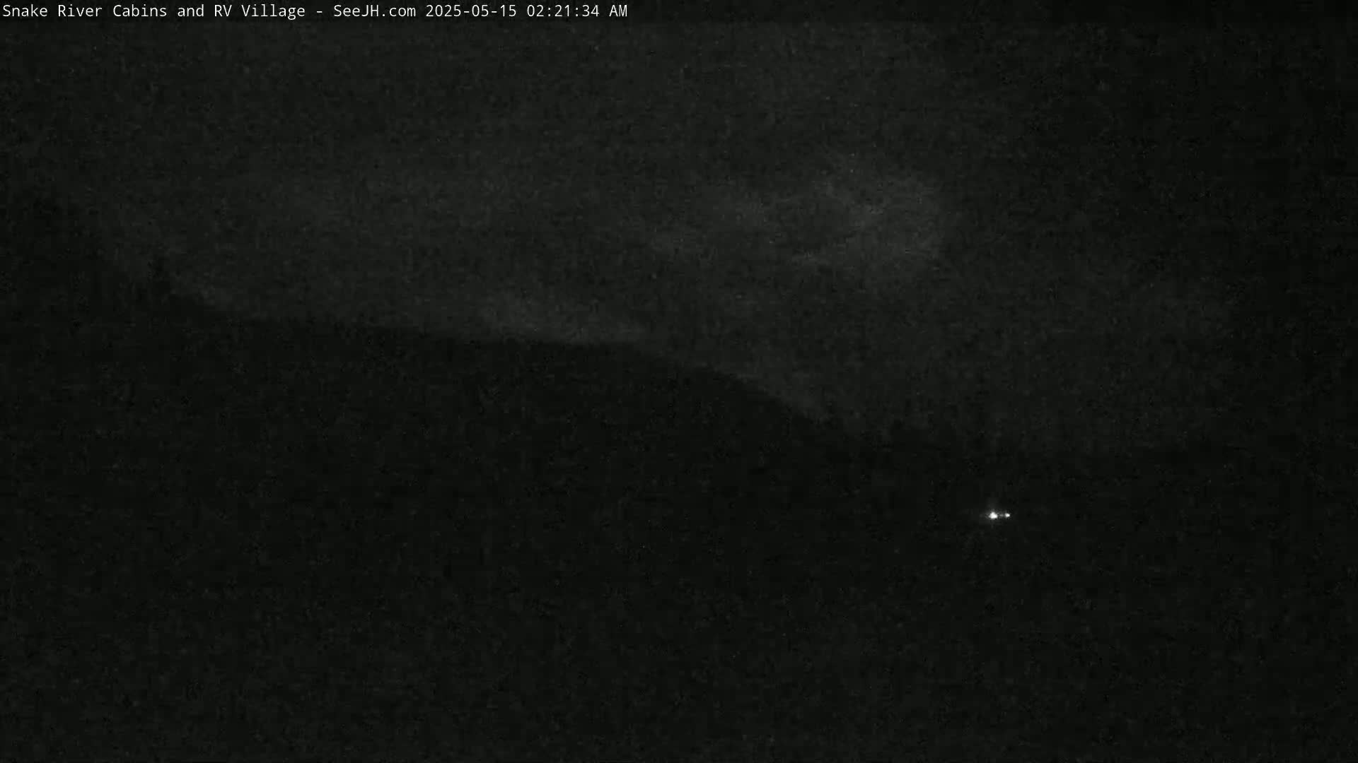 A nighttime, low-light image shows a dark landscape with a faint, hazy light source in the middle distance and two very small points of light at the bottom.