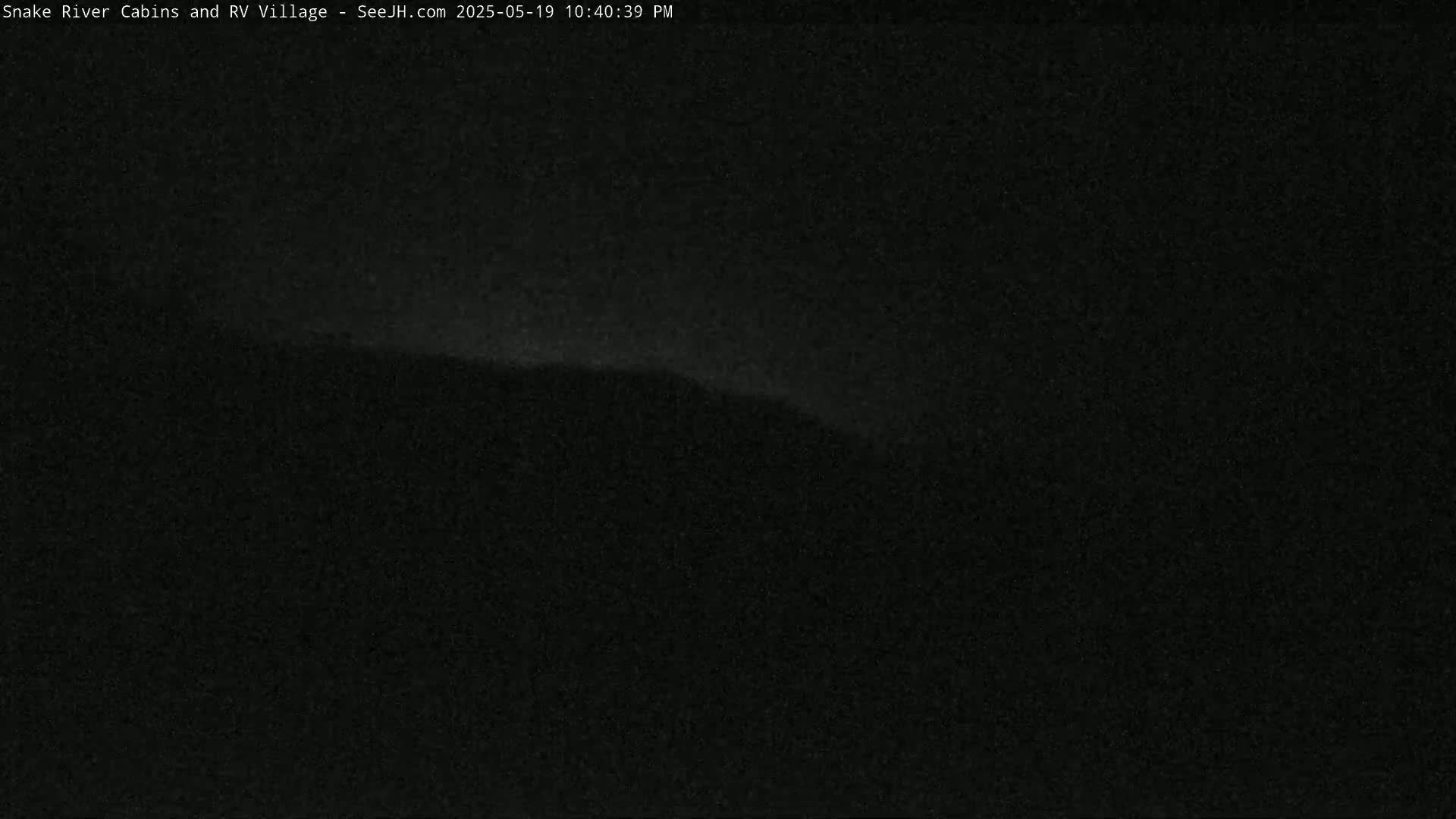 A dark, nighttime outdoor scene shows a dimly lit hill or ridge in the distance under a mostly clear sky.