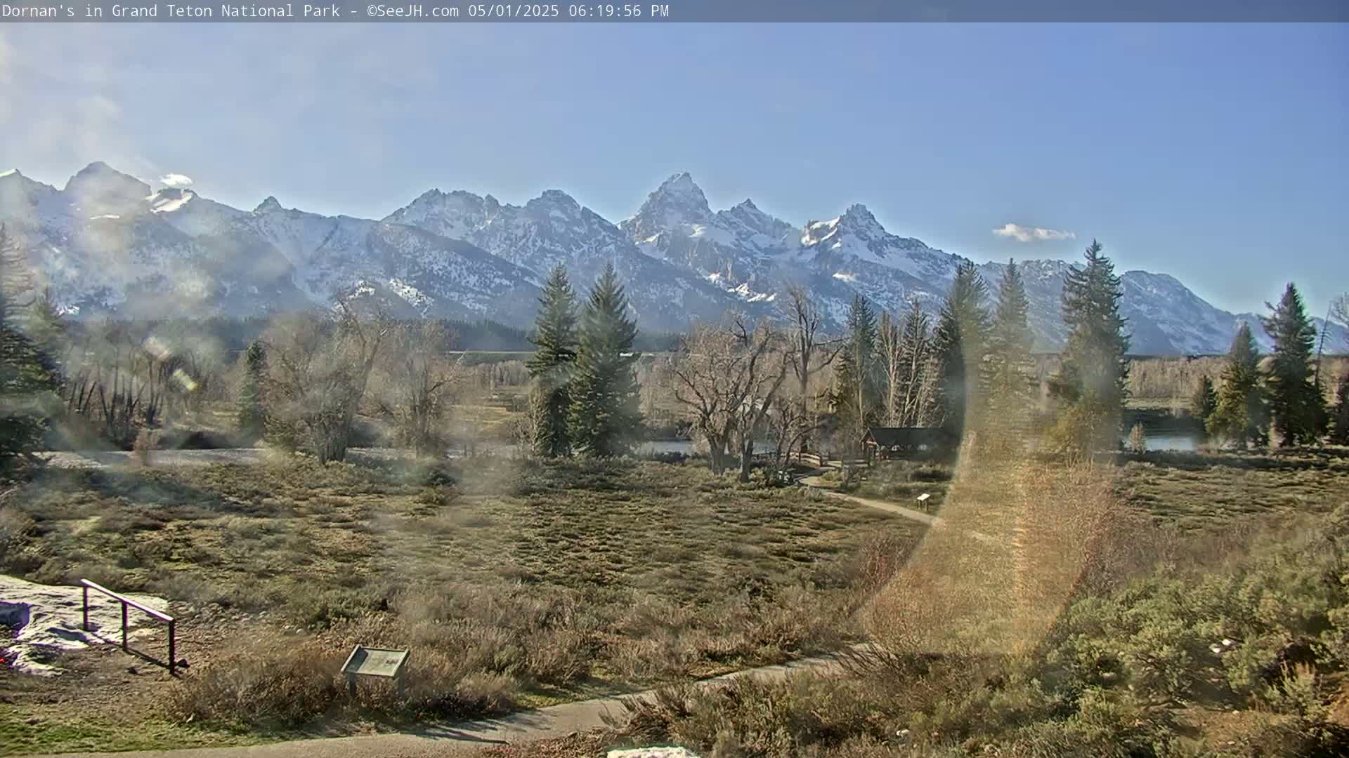 A snow-capped mountain range rises in the background of a flat, scrubby landscape under a clear, sunny sky.