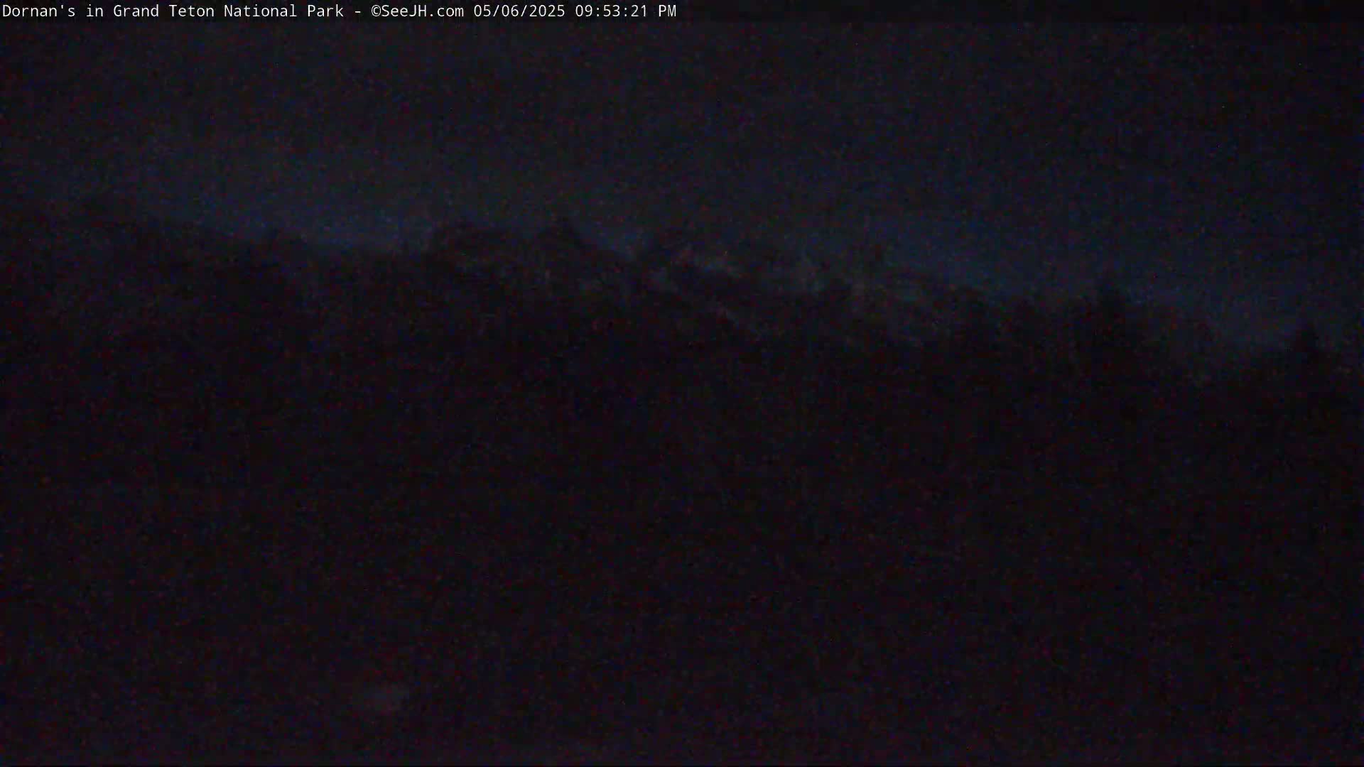 A dark, nighttime view shows a silhouetted mountain range under a mostly clear, dark blue sky.