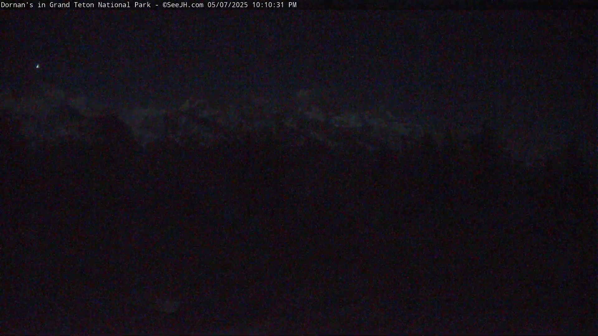A dark, nighttime view shows faintly illuminated mountain peaks under a mostly clear sky.