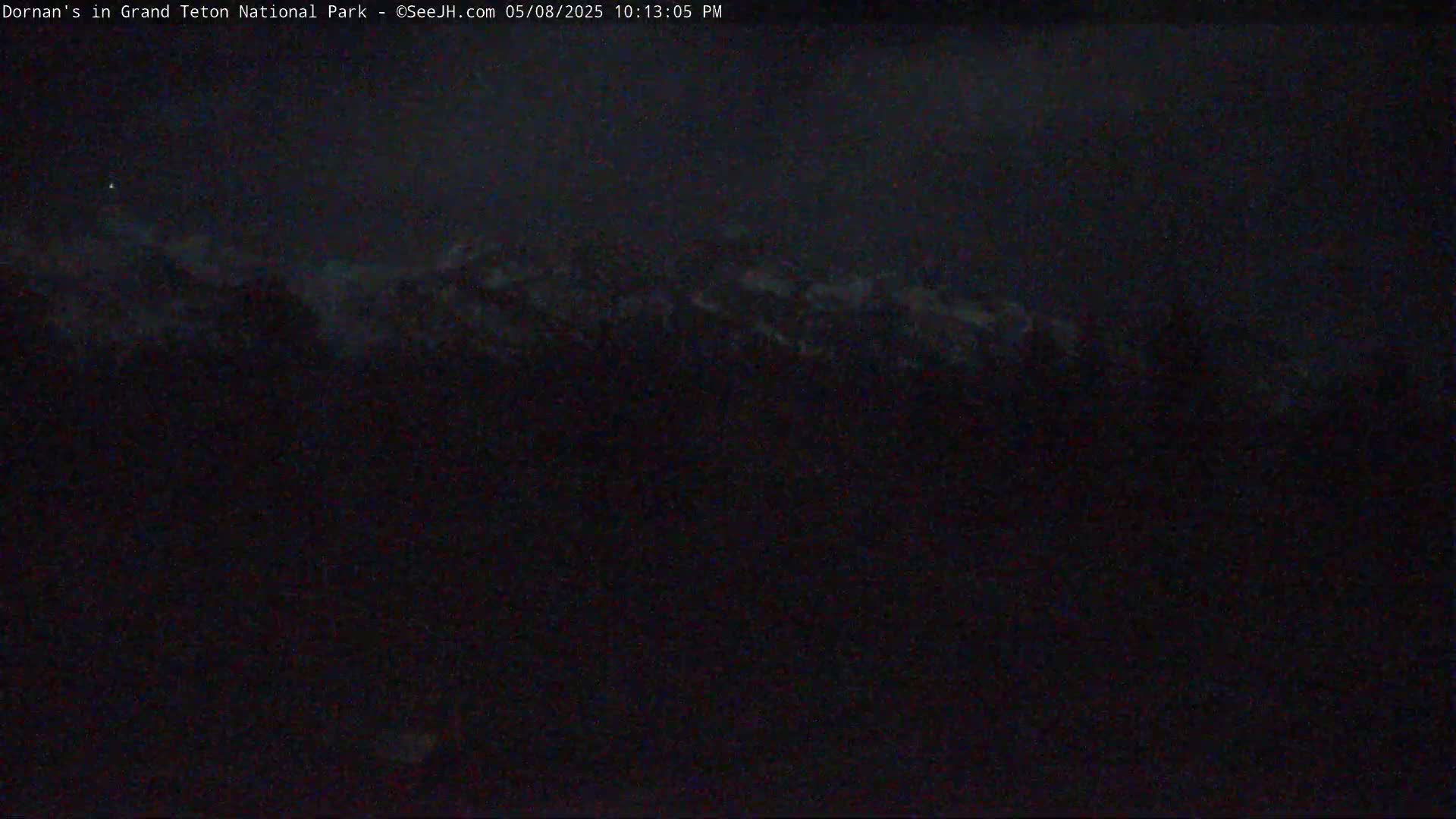 A dark, nighttime landscape shows faintly illuminated mountains under a cloudy sky.