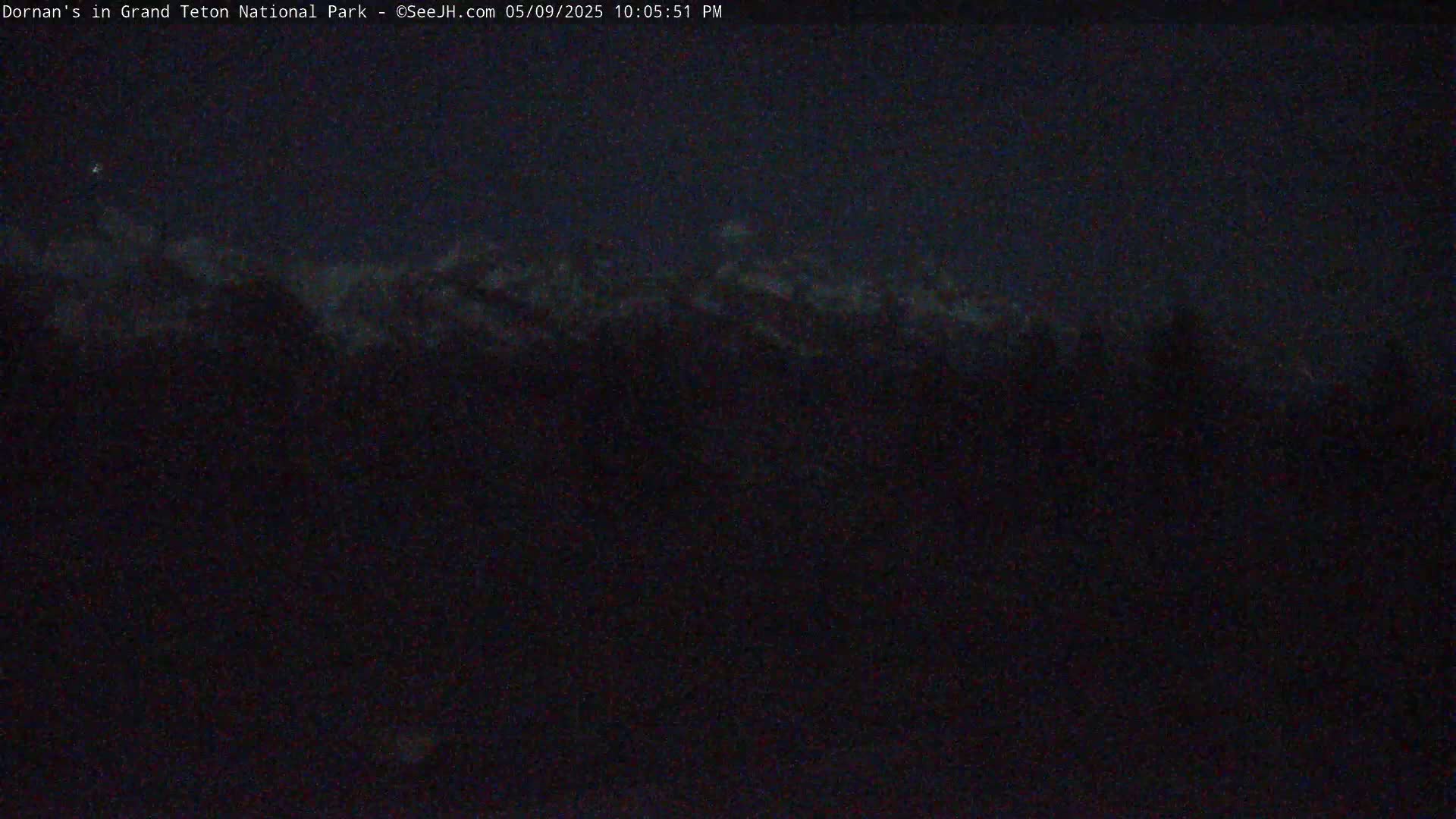 A dark, nighttime view of faintly visible mountaintops under a mostly cloudy sky.