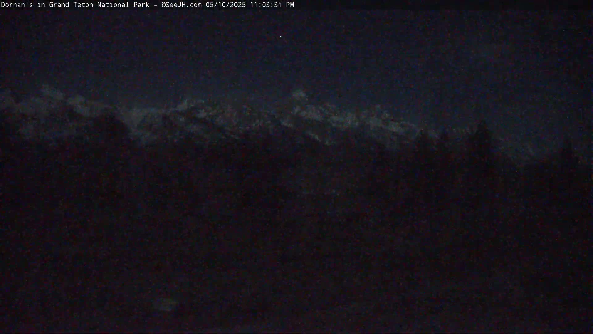 A nighttime view of snow-capped mountains silhouetted against a dark sky.