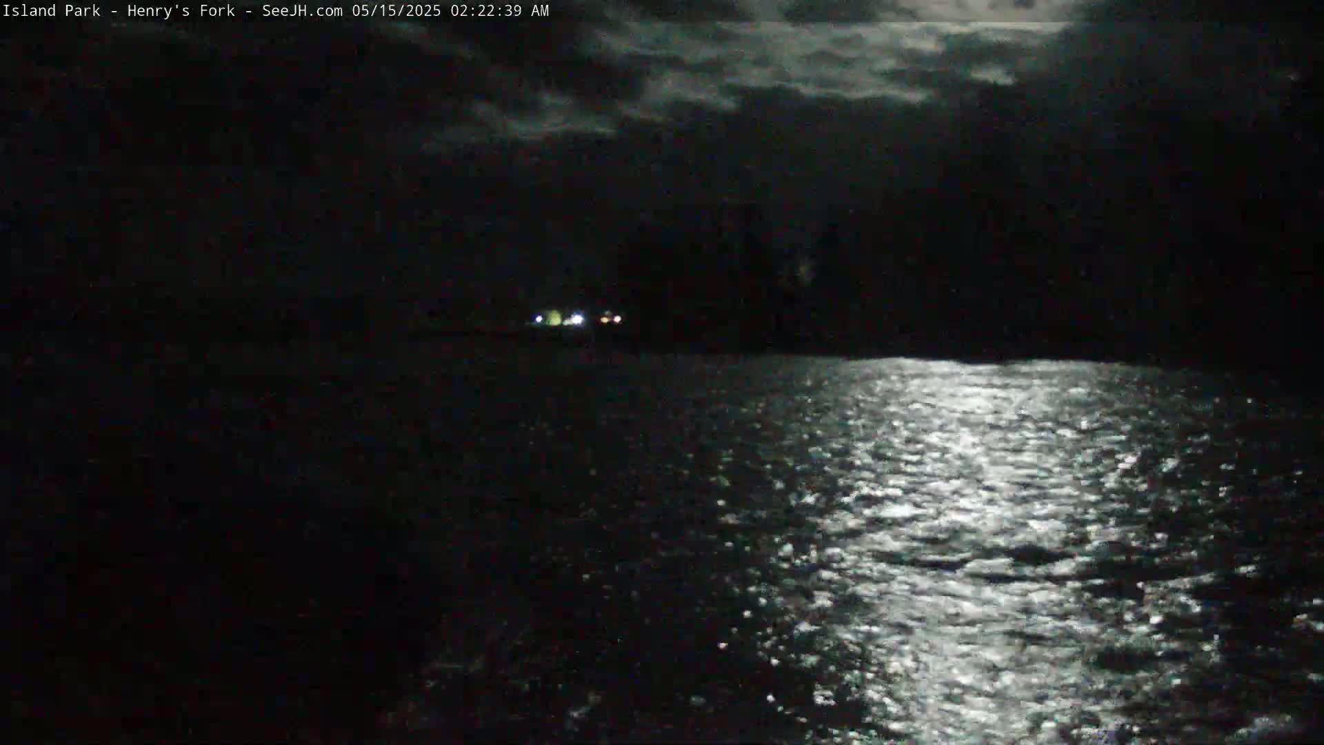 A moonlit, nighttime view of dark water reflecting light, with a dark shoreline visible in the distance.
