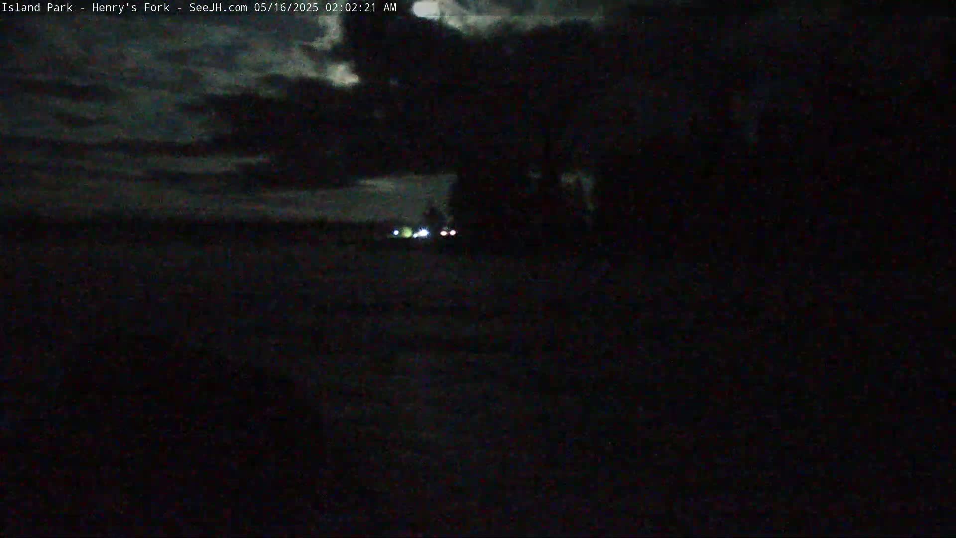 A dark, nighttime scene shows a few faint lights in the distance under a cloudy sky.