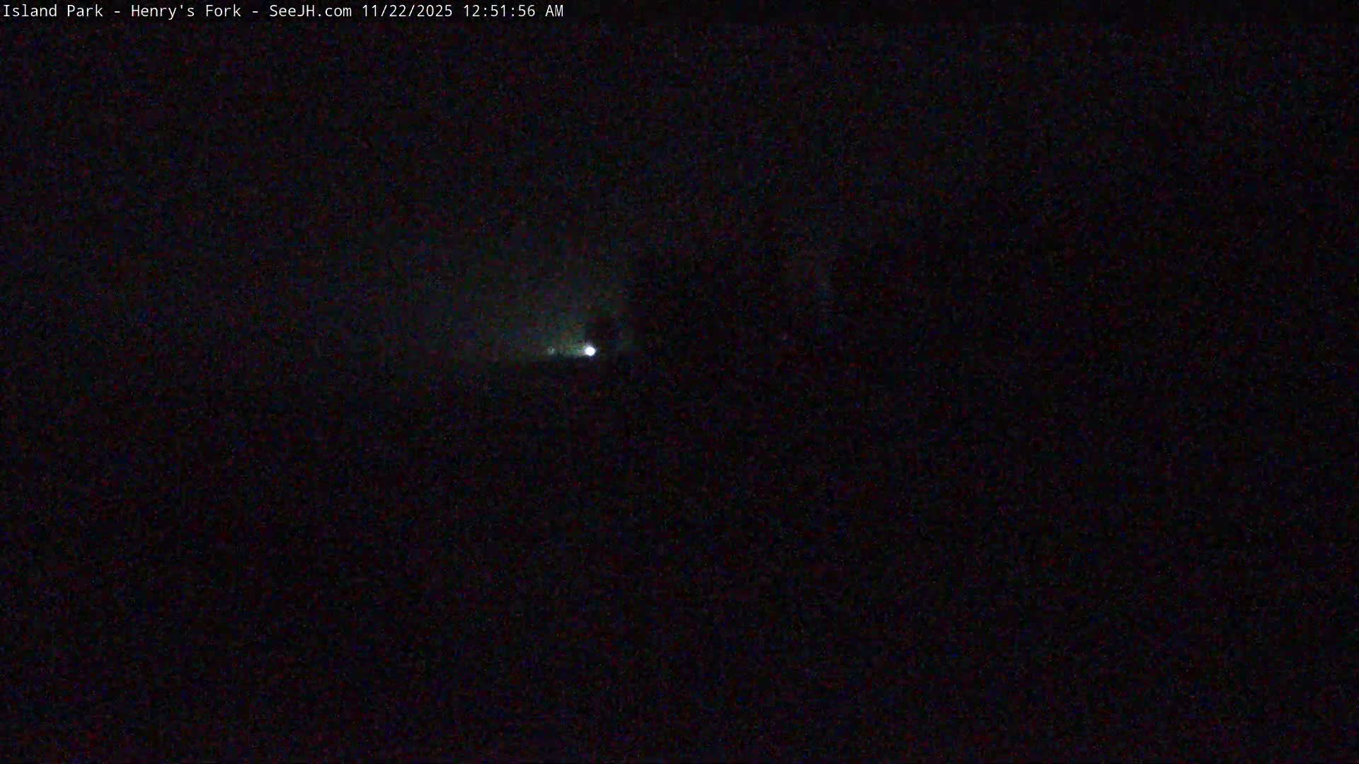 A dark, nighttime outdoor scene is illuminated by a single bright white light with a faint green-blue halo visible in the mid-left portion of the frame.