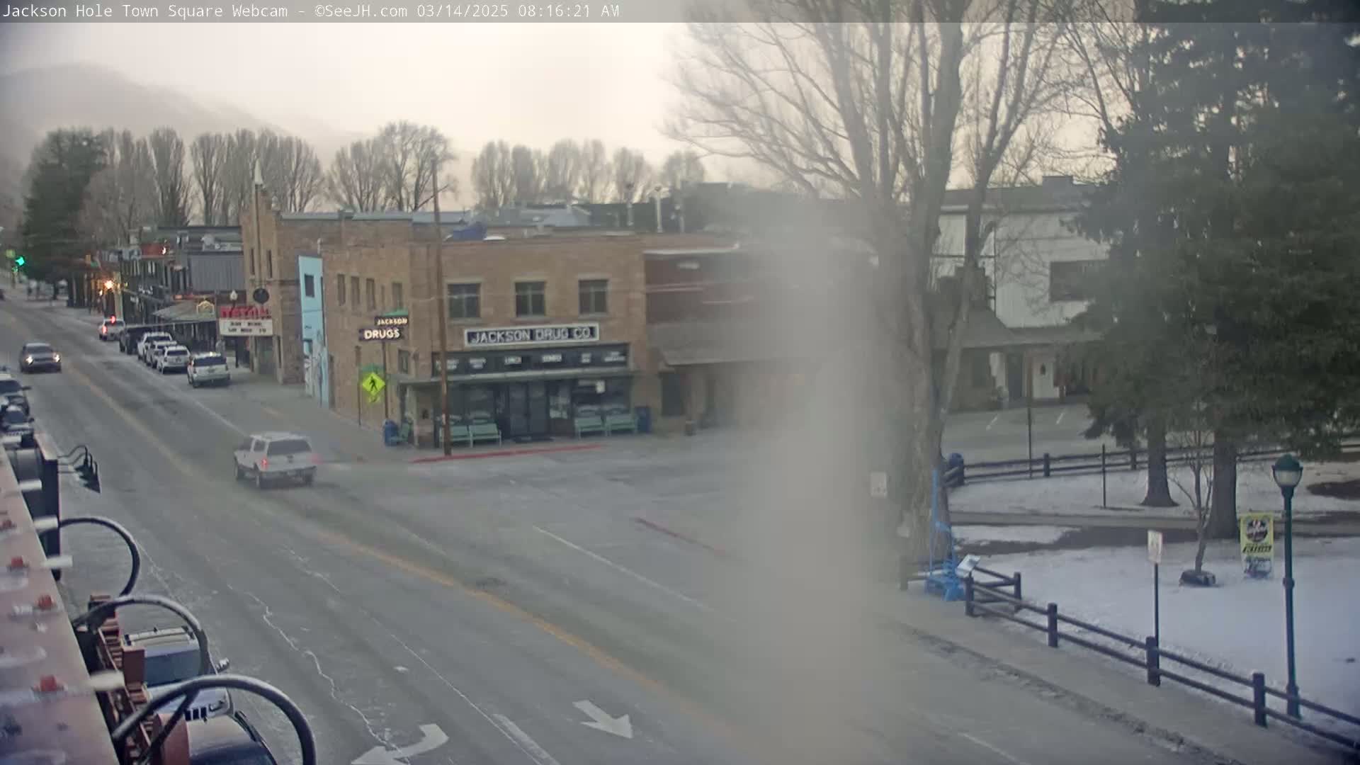 A hazy, overcast morning reveals a town square with sparse traffic on a street lined with buildings, including one that says "Jackson Drug Co." on it, and a small snow-covered park.