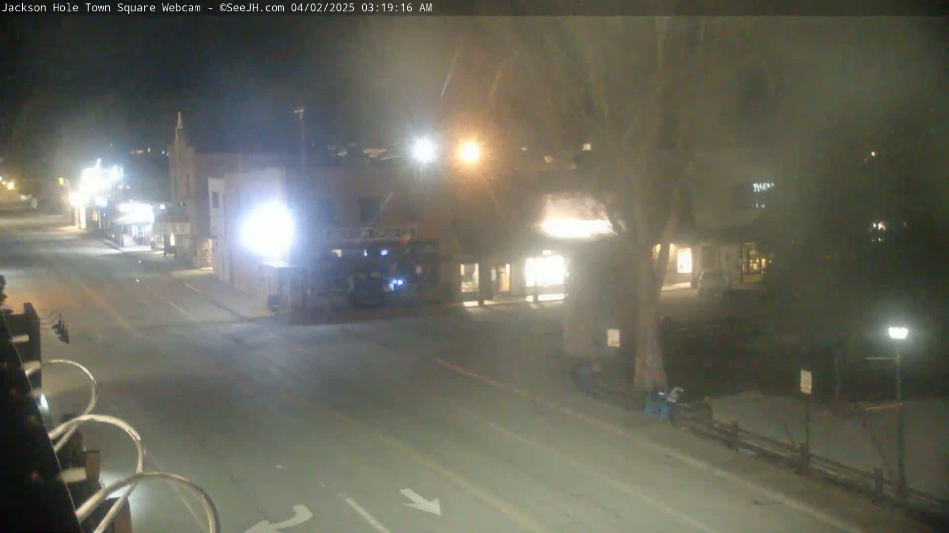 A nighttime view of a mostly empty town square with several buildings illuminated, under hazy conditions.