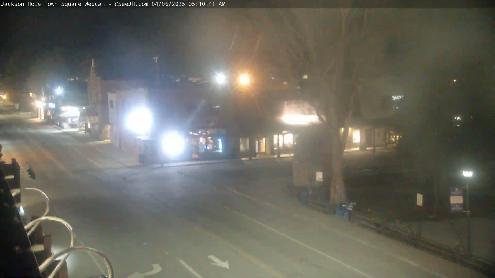 A nighttime, slightly hazy view of a town square with a street, buildings, and some trees.