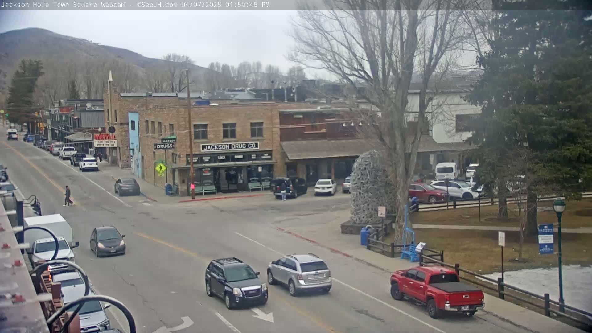A street scene in a town shows several cars, pedestrians, and buildings on an overcast day.