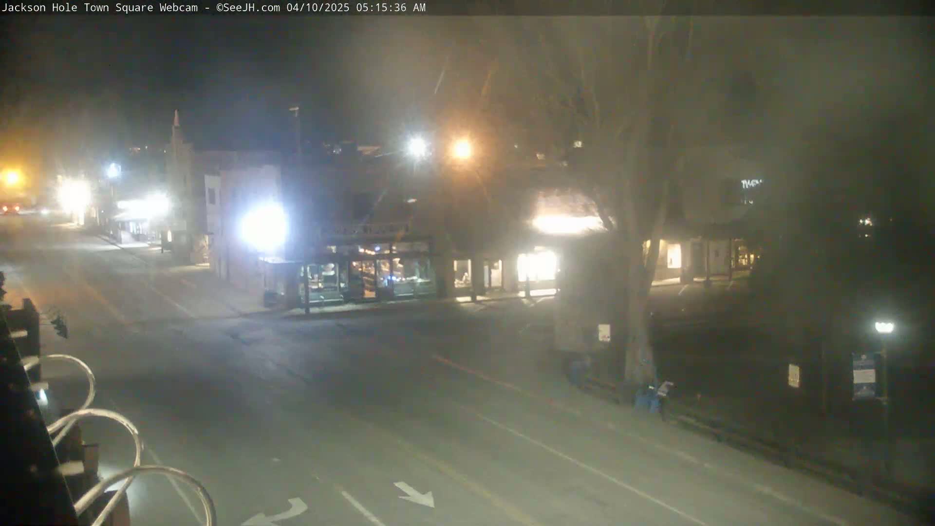 A mostly empty town square at night, under hazy conditions, with some buildings and streetlights visible.