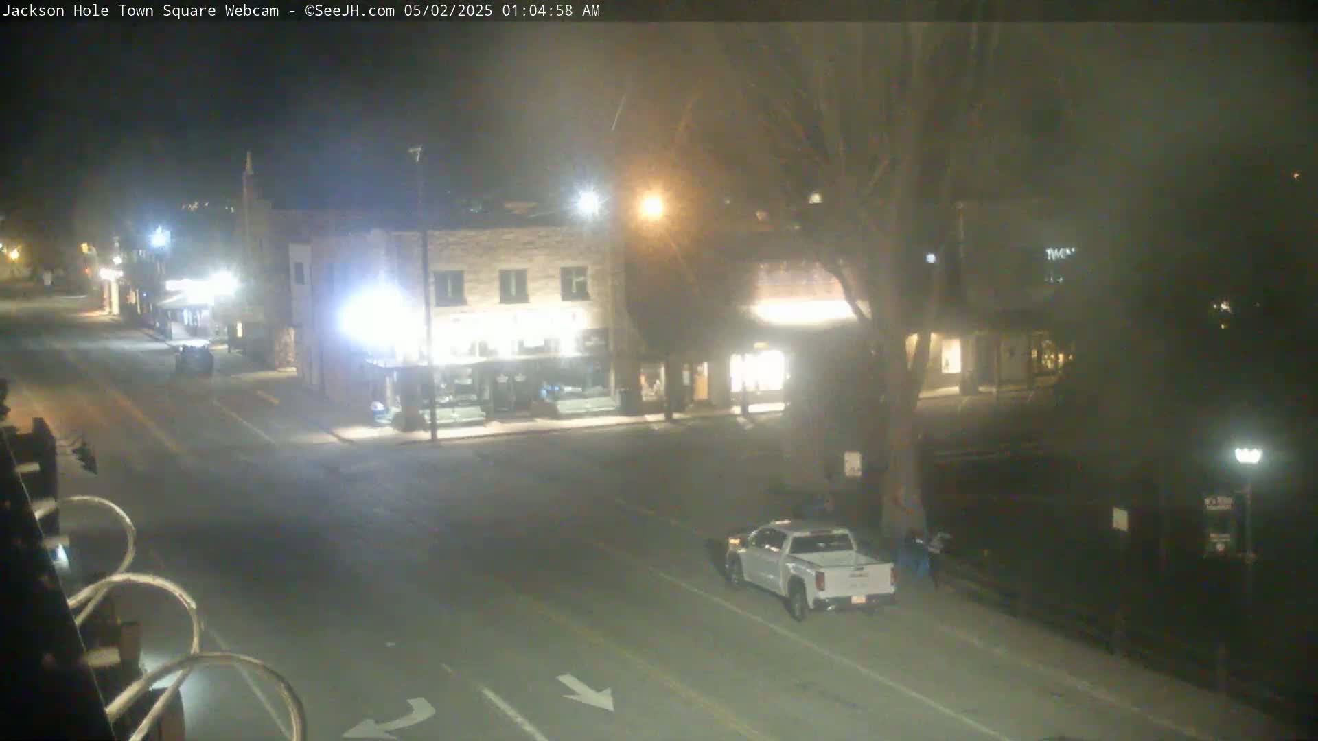 A mostly empty street at night, with a few buildings and a lone white truck visible under hazy conditions.