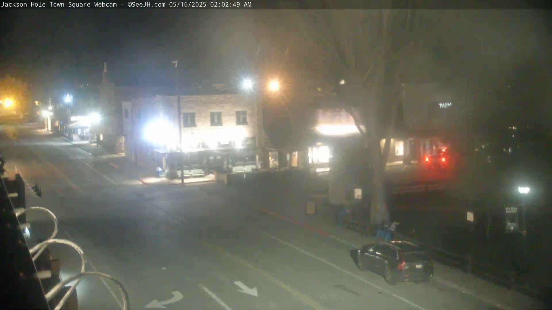 A foggy night scene shows a mostly empty street in front of some buildings, with a few cars and people visible.