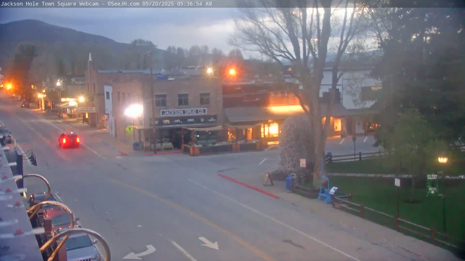 A mostly empty town square at twilight, with a few cars and people visible, under a partly cloudy sky.