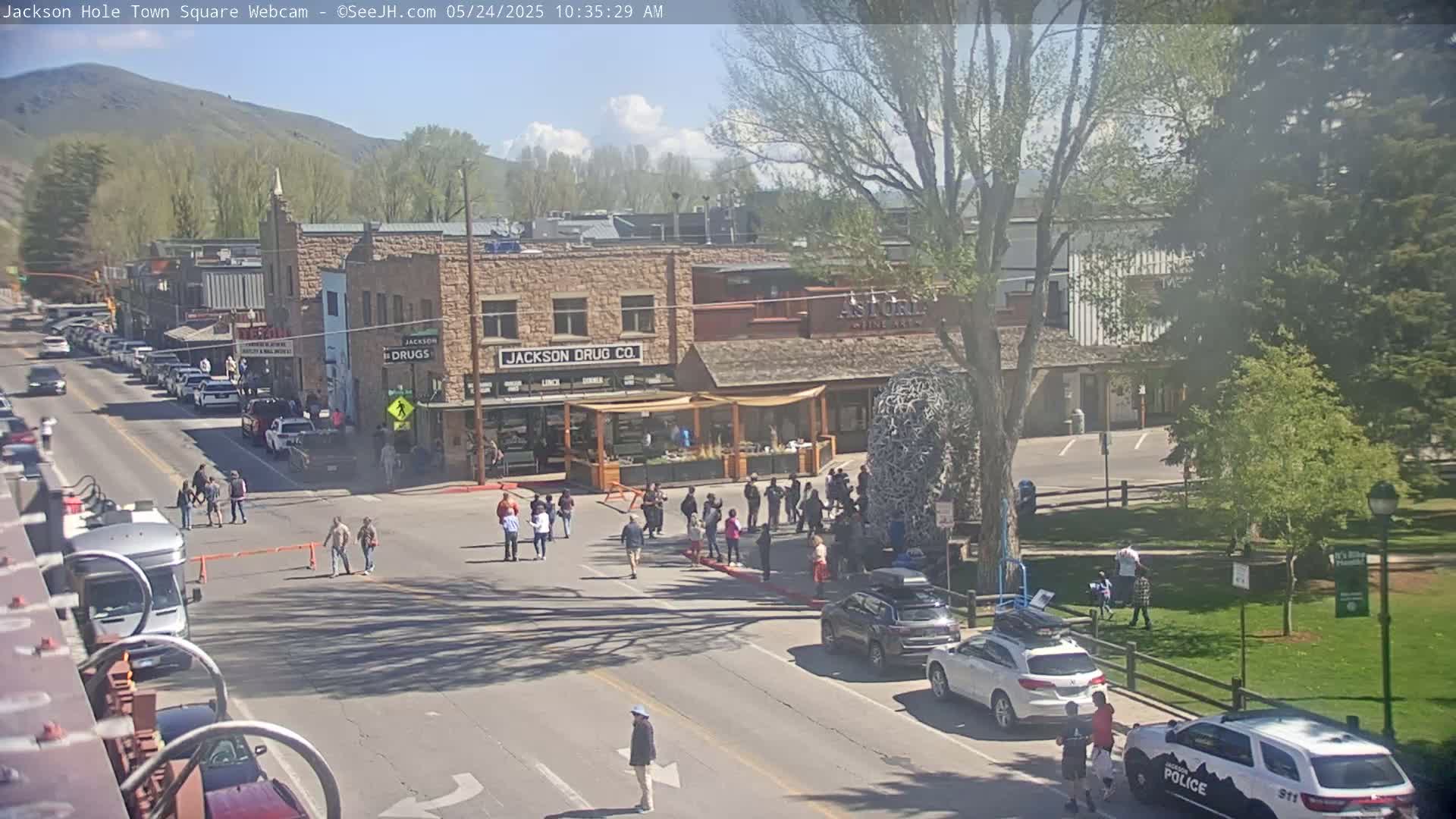 A partly sunny town square scene shows several pedestrians, parked cars, and buildings, including a drug store.