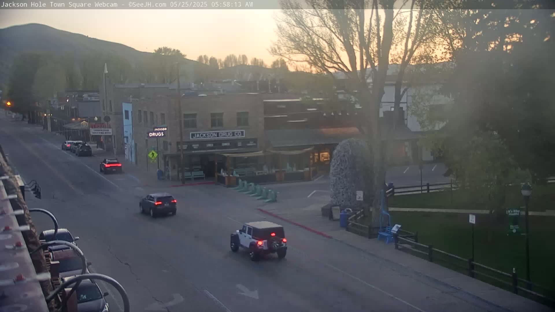 A hazy sunrise illuminates a town square with several cars on the road, and a few buildings, including one labeled "Jackson Drug Co." visible.