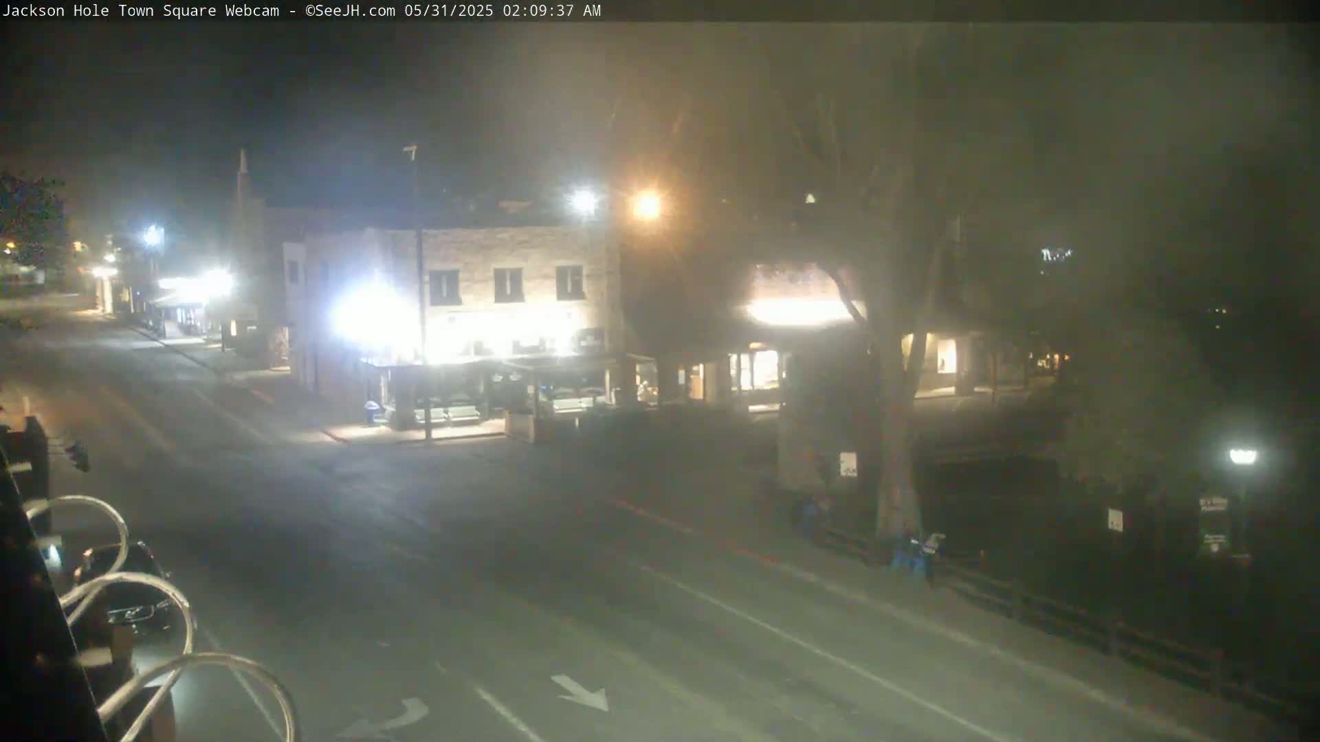A nighttime view of a mostly empty town square with two buildings and a street, under hazy conditions.