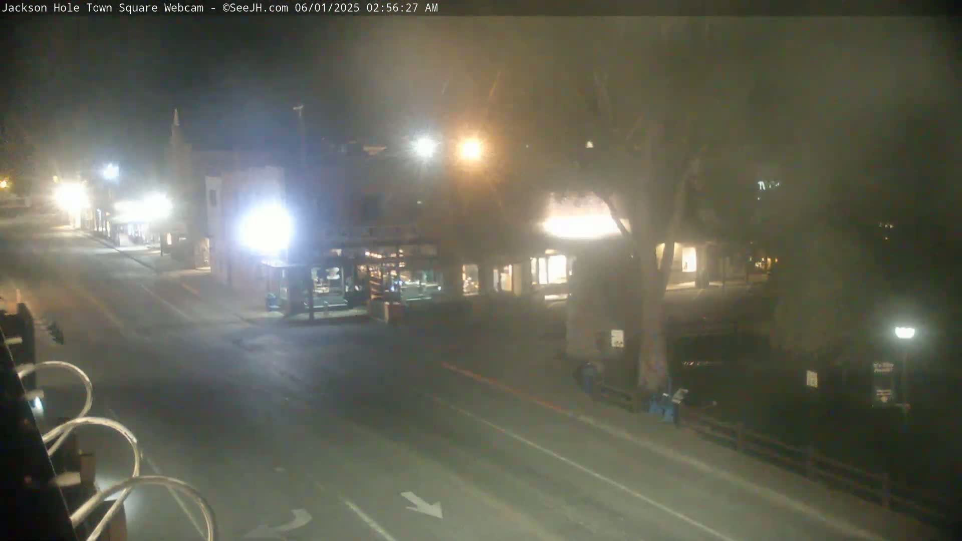 A mostly empty, dimly lit street at night shows a few buildings and some pedestrians.