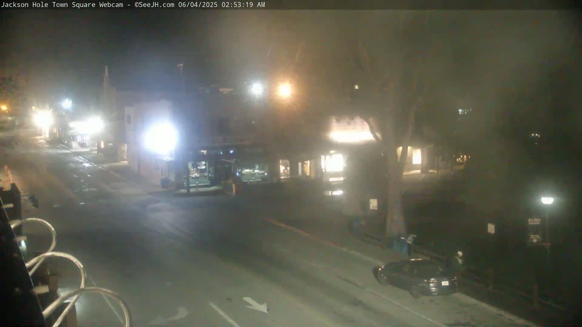 A mostly empty town square at night, slightly hazy with some streetlights and a few vehicles visible.