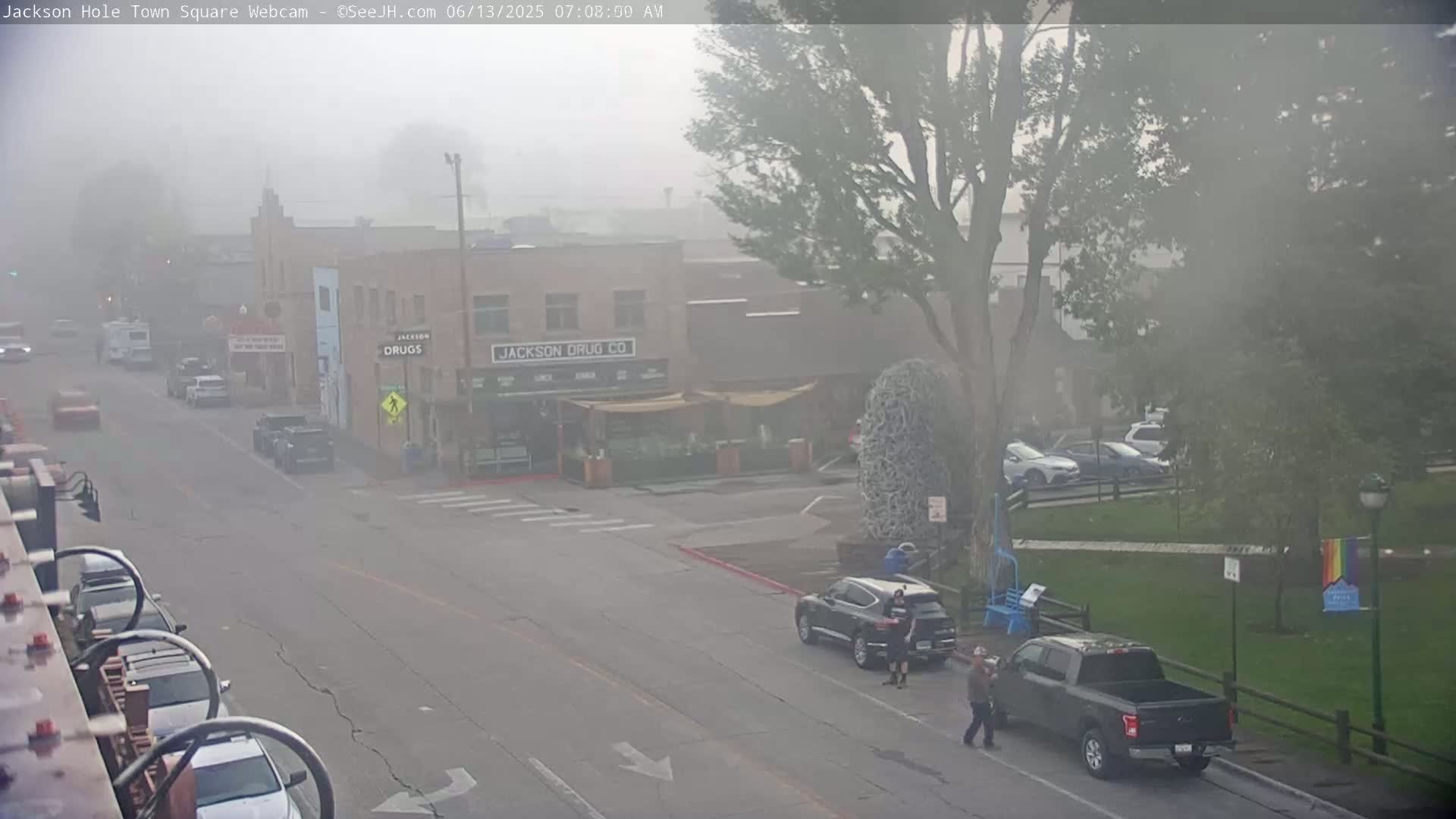 A foggy town square scene shows a street with parked and driving cars, a few pedestrians, and buildings, including one with "Jackson Drug Co." visible on its facade.