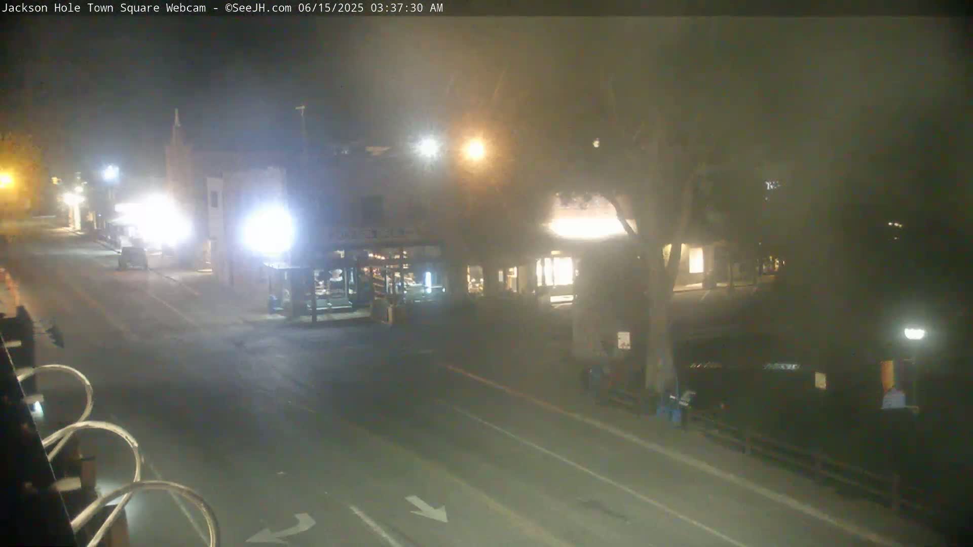 A mostly empty town square at night is dimly lit by streetlights and building lights in hazy conditions.