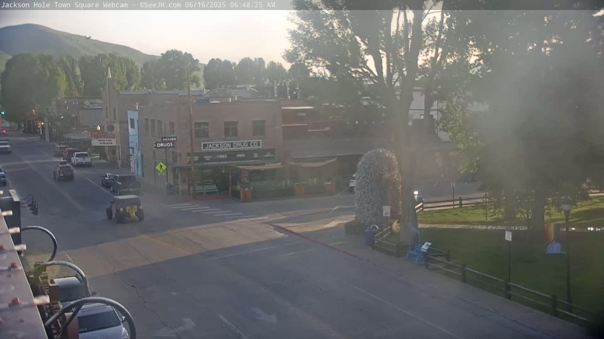 A hazy morning view of a town square with cars on the road, buildings, and a park-like area with trees.