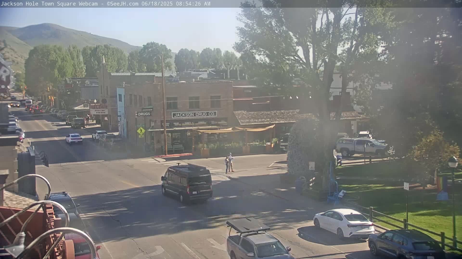 A sunny town square with several cars and trucks on the street, a building labeled "Jackson Drug Co," and a grassy area in the background.