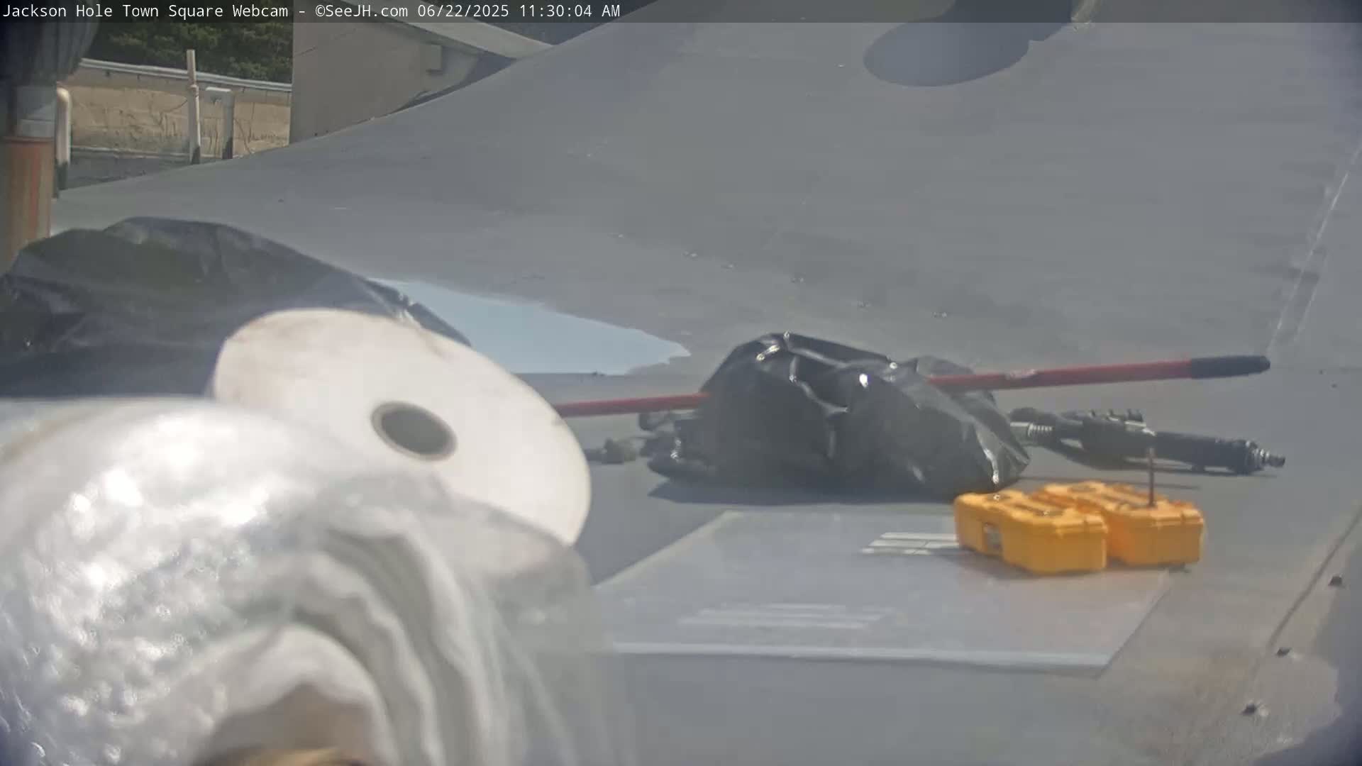 Several large spools of material, black trash bags, a long-handled tool, and two small yellow toolboxes lie on a gray surface outdoors on a sunny day.