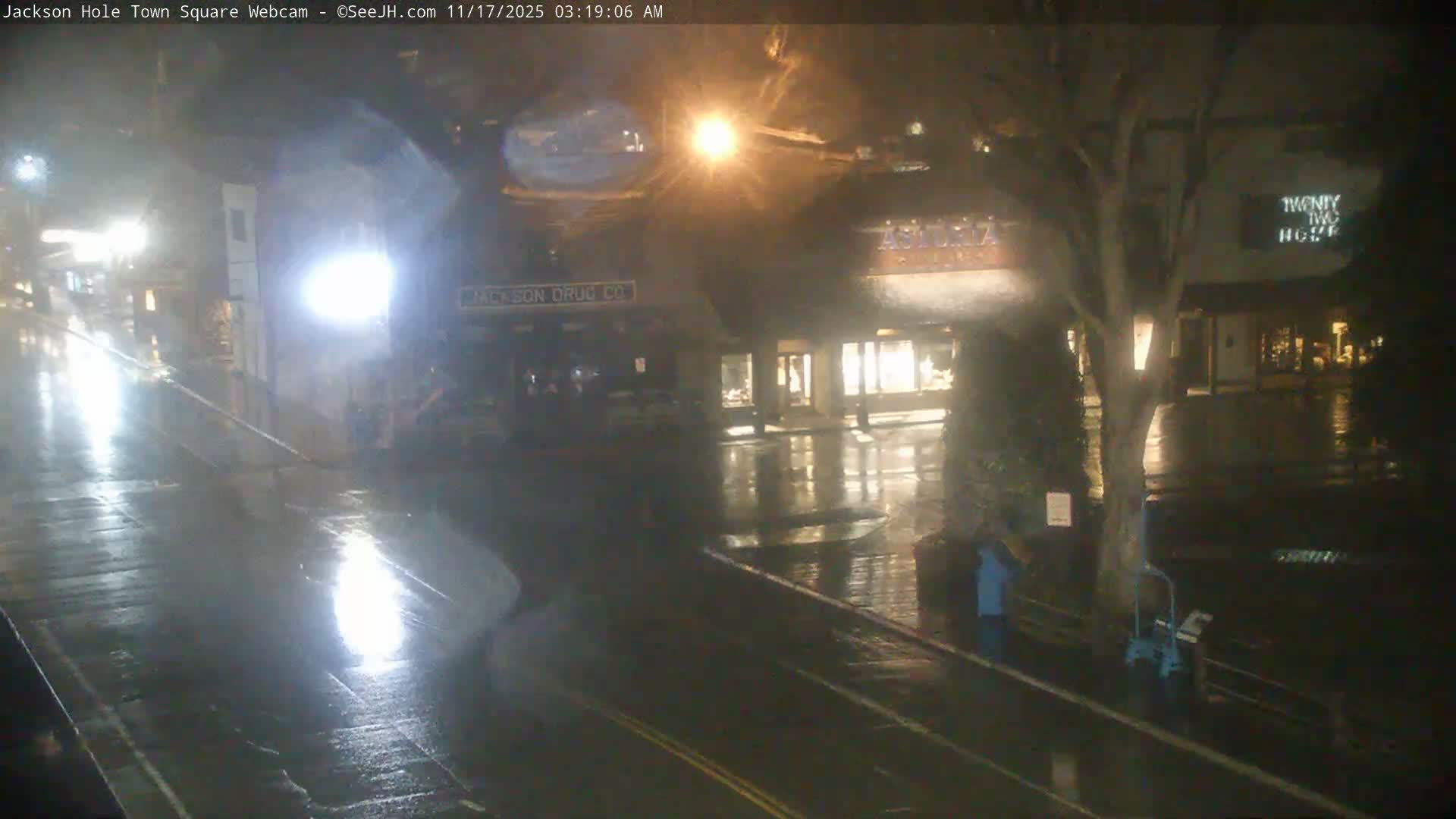 A wet street and buildings are illuminated by streetlights and interior lights on a rainy night.