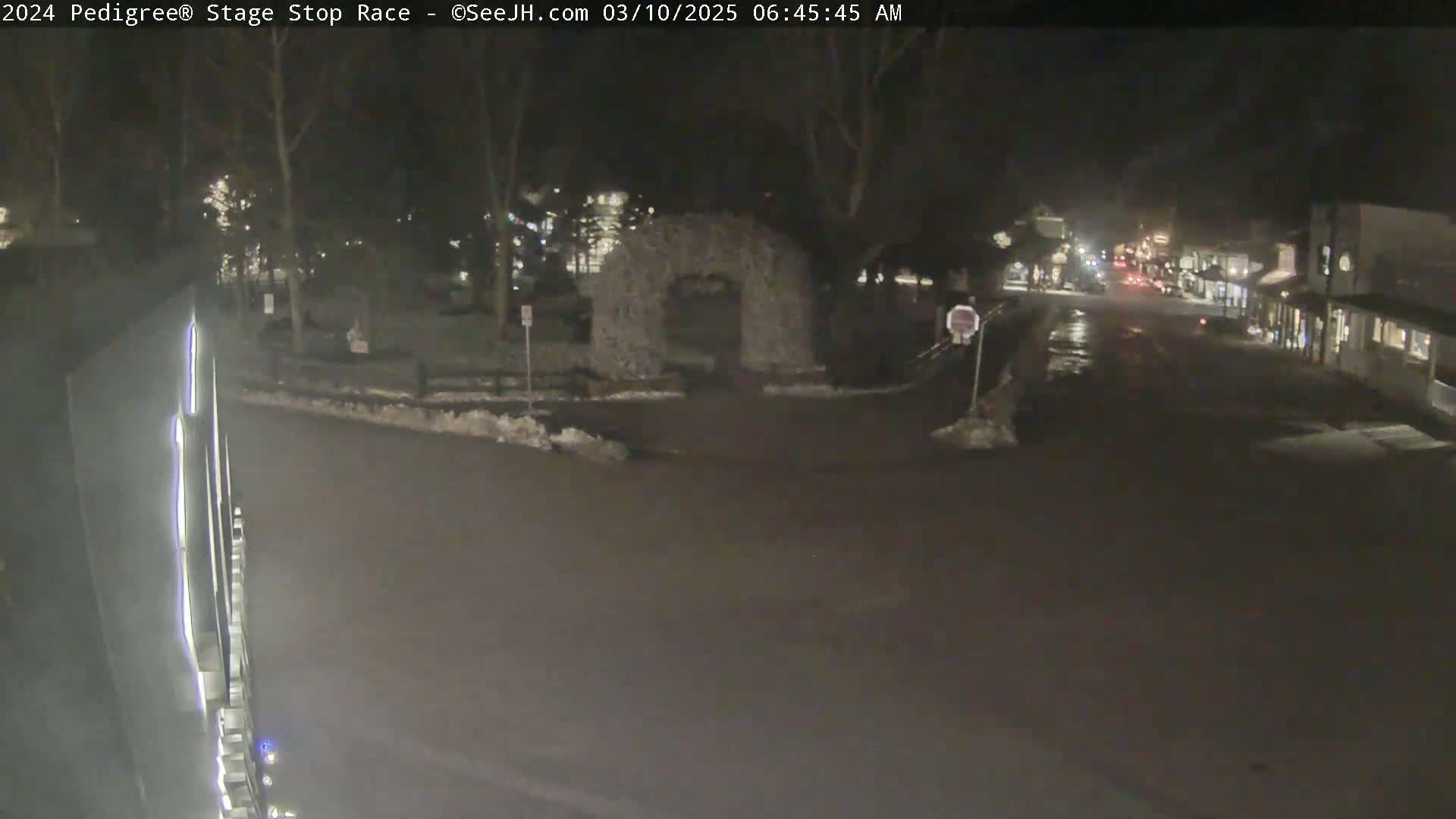 A nighttime street scene shows a mostly empty road with a stone archway and some snow on the ground.