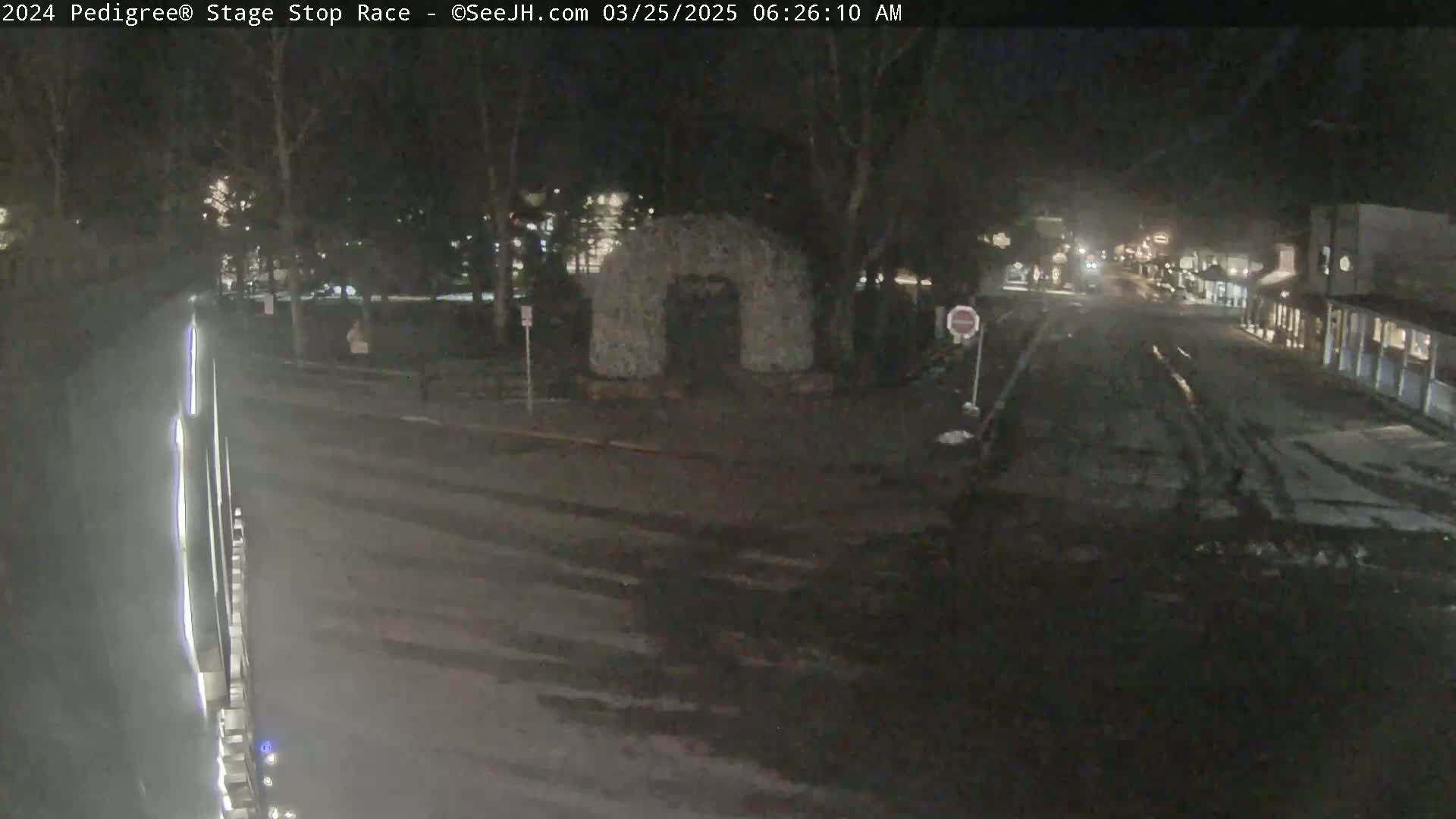 A nighttime street scene shows a mostly empty road with a stone archway in the middle, under dark, possibly overcast conditions.