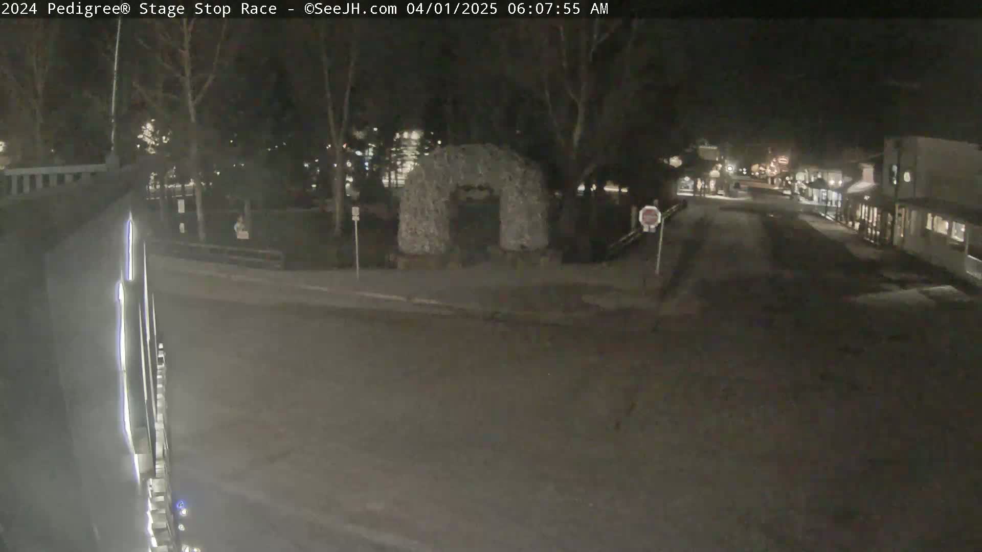 A nighttime street scene shows a dark road leading to a building, with trees and a stone archway visible in the background.