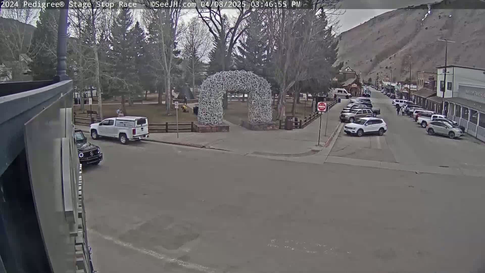 A town square with a large antler archway, several parked cars, and a few people is visible on an overcast day.