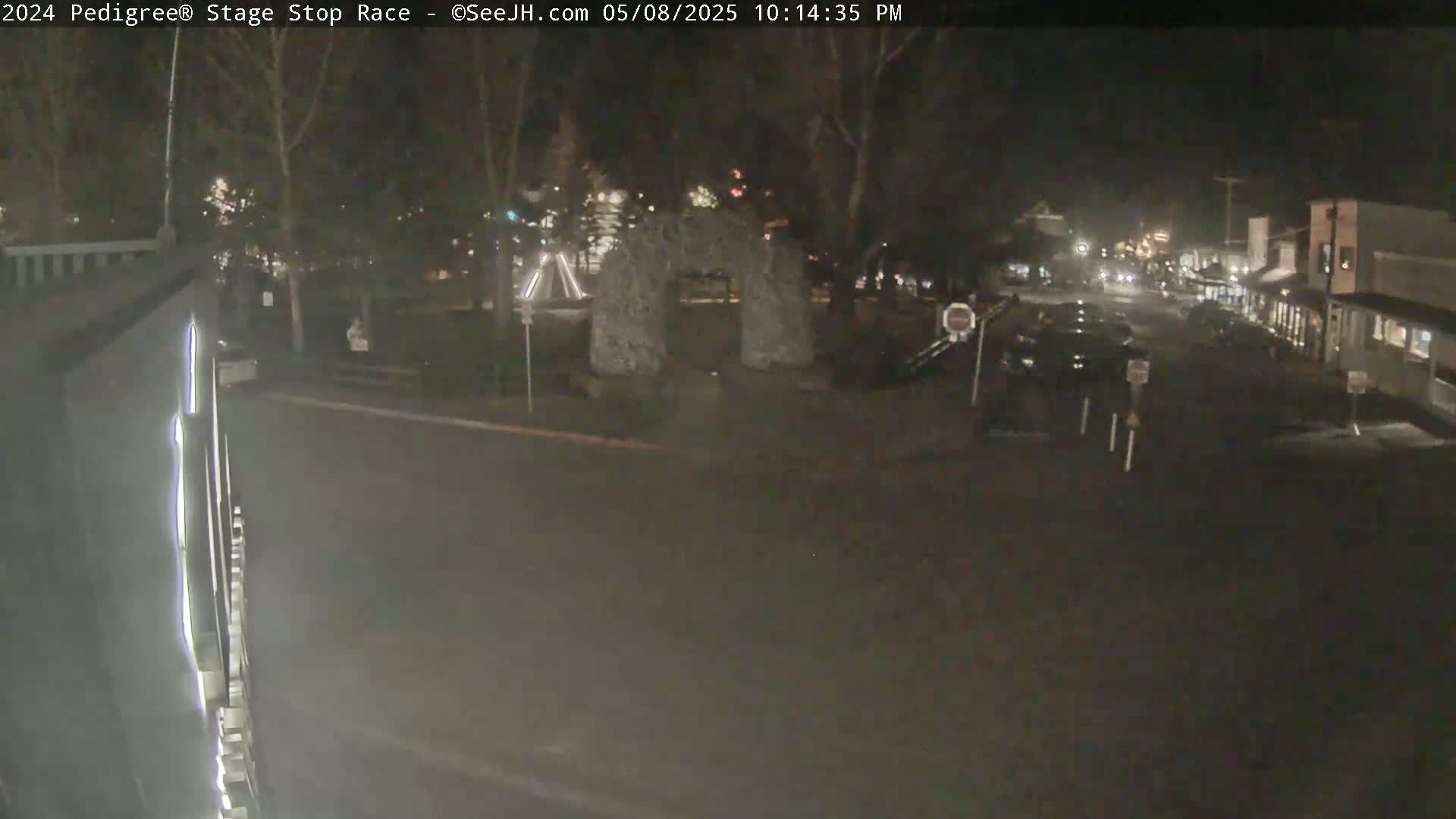 A nighttime view of a mostly empty street with parked cars and a stone archway in the background under dark, clear skies.