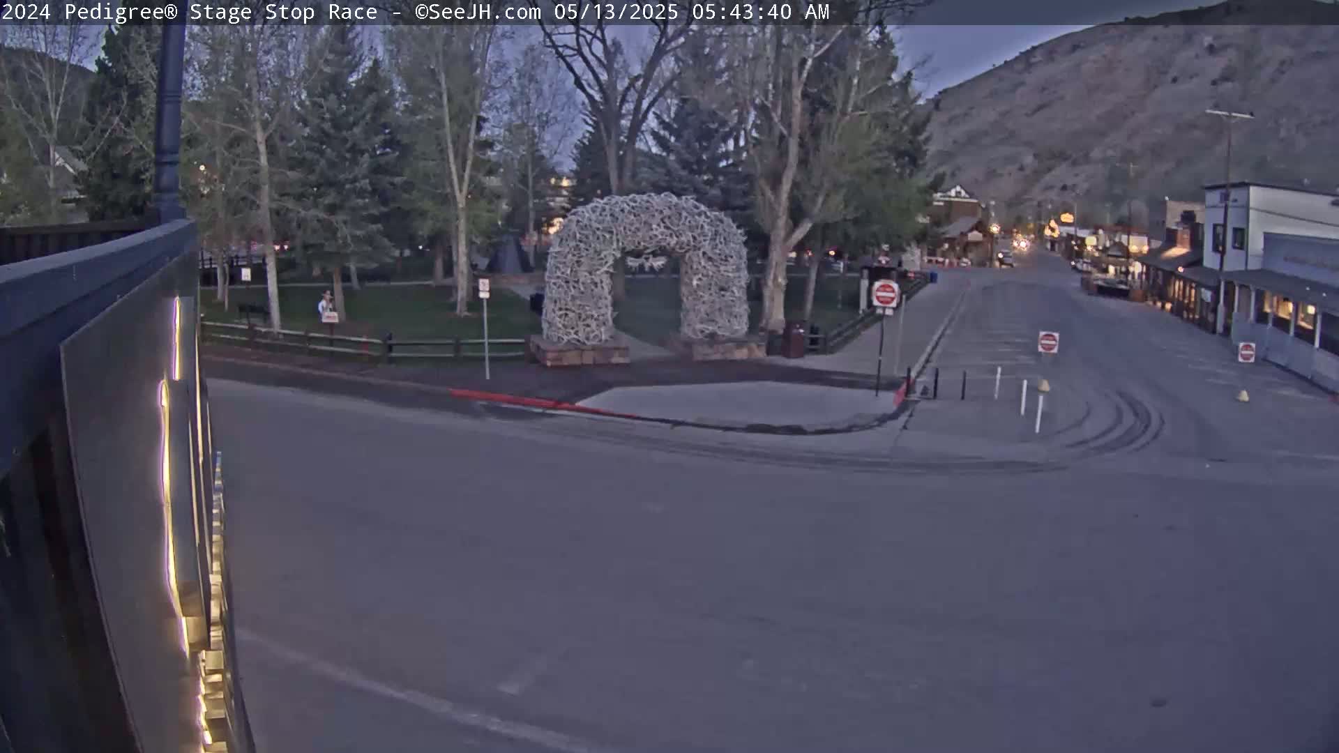 A mostly empty town square at dusk, featuring a large antler archway, is visible from a street corner.