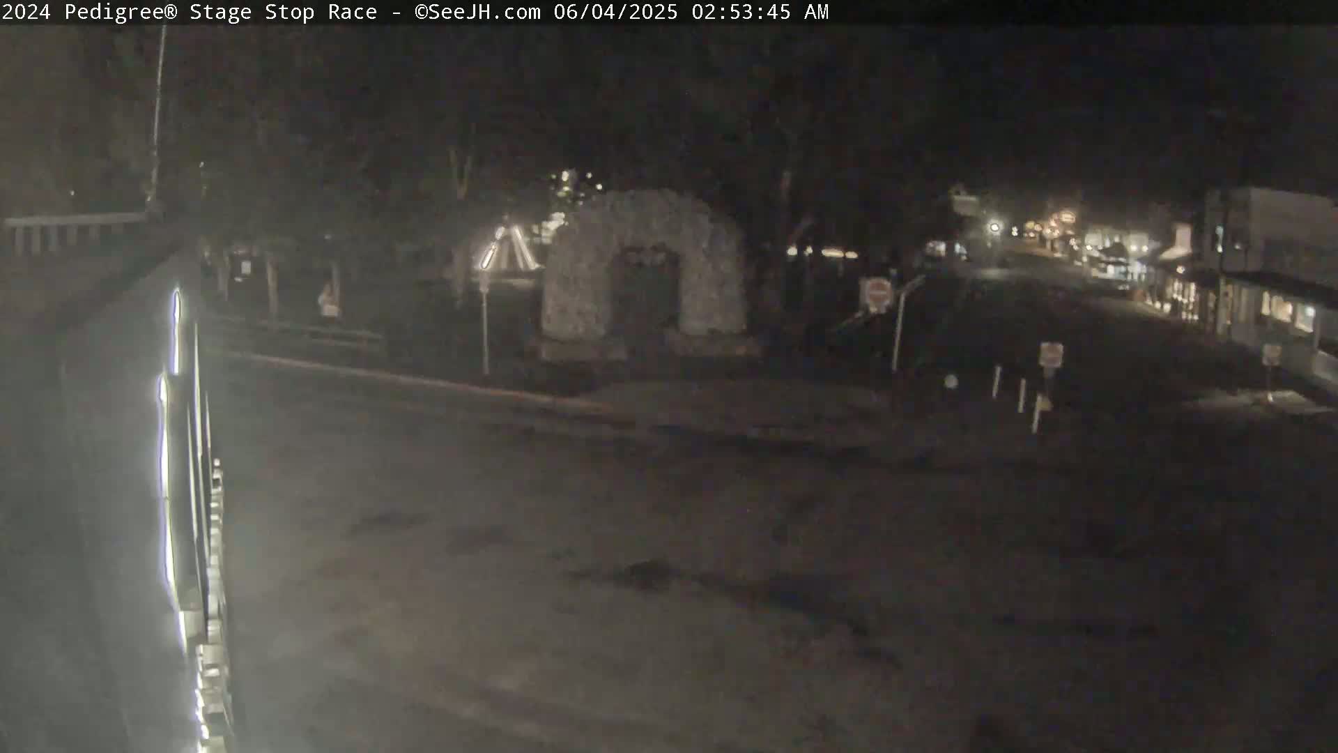 A nighttime, low-light view of a mostly empty street and intersection, with a stone structure visible in the mid-ground.