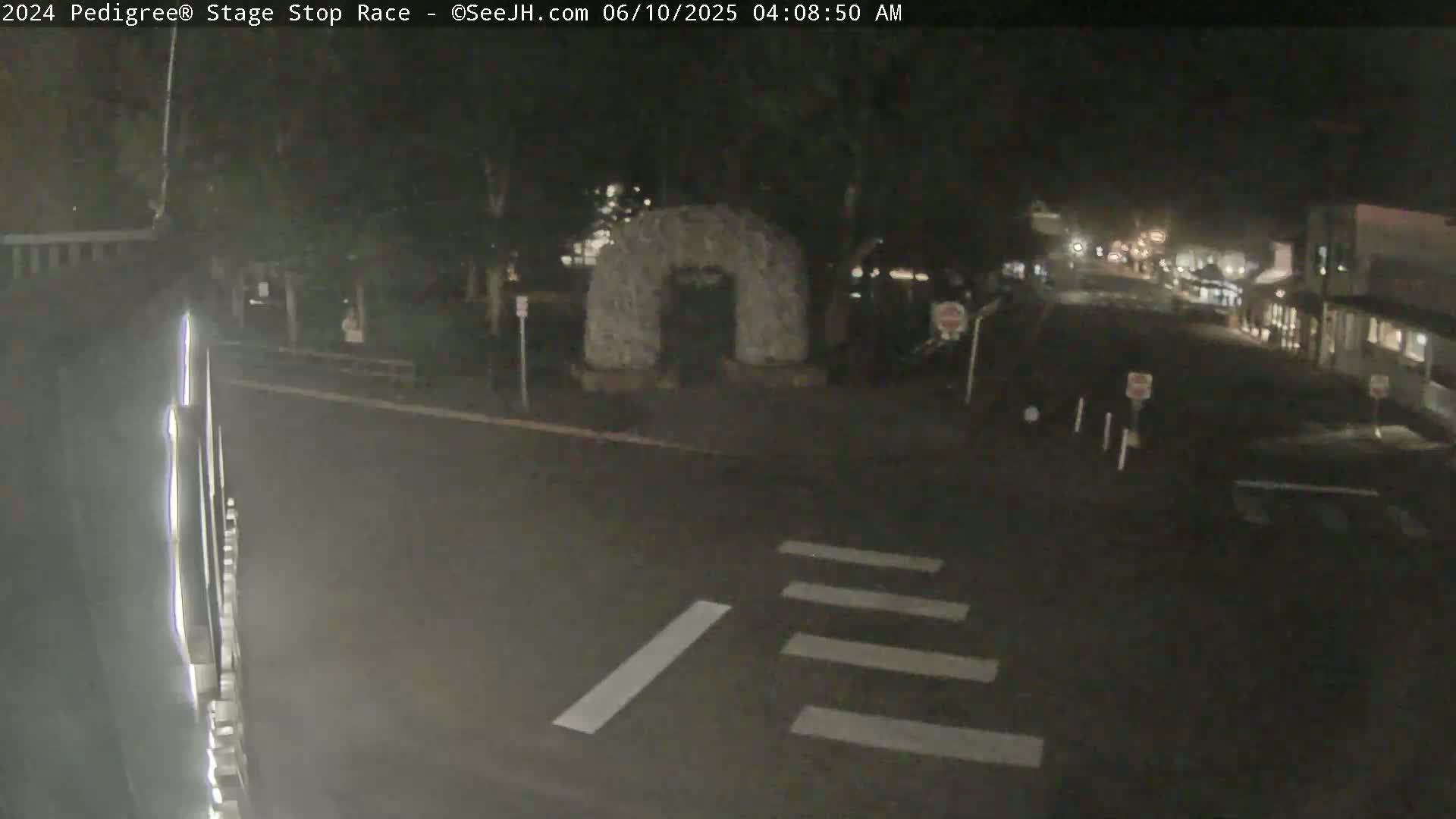 A nighttime, low-light view of a street intersection with a stone archway in the background, and a crosswalk visible in the foreground.